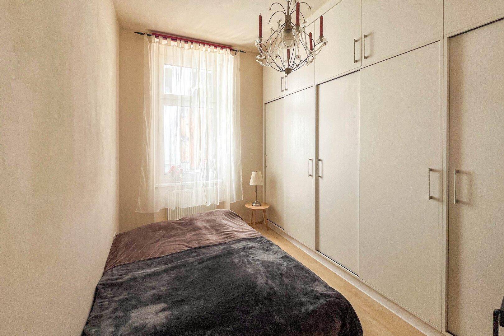Gemütliches Schlafzimmer mit Einbauschränken, Einzelbett und Kronleuchter.