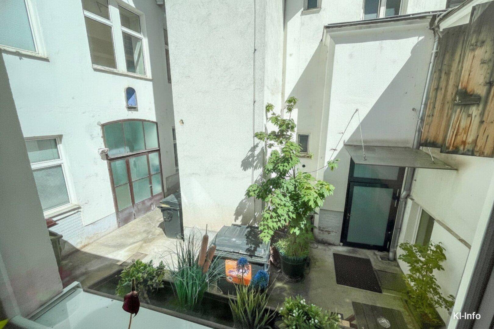 Blick von oben in einen hellen Innenhof mit Pflanzen und Zugang zu den Gebäuden.