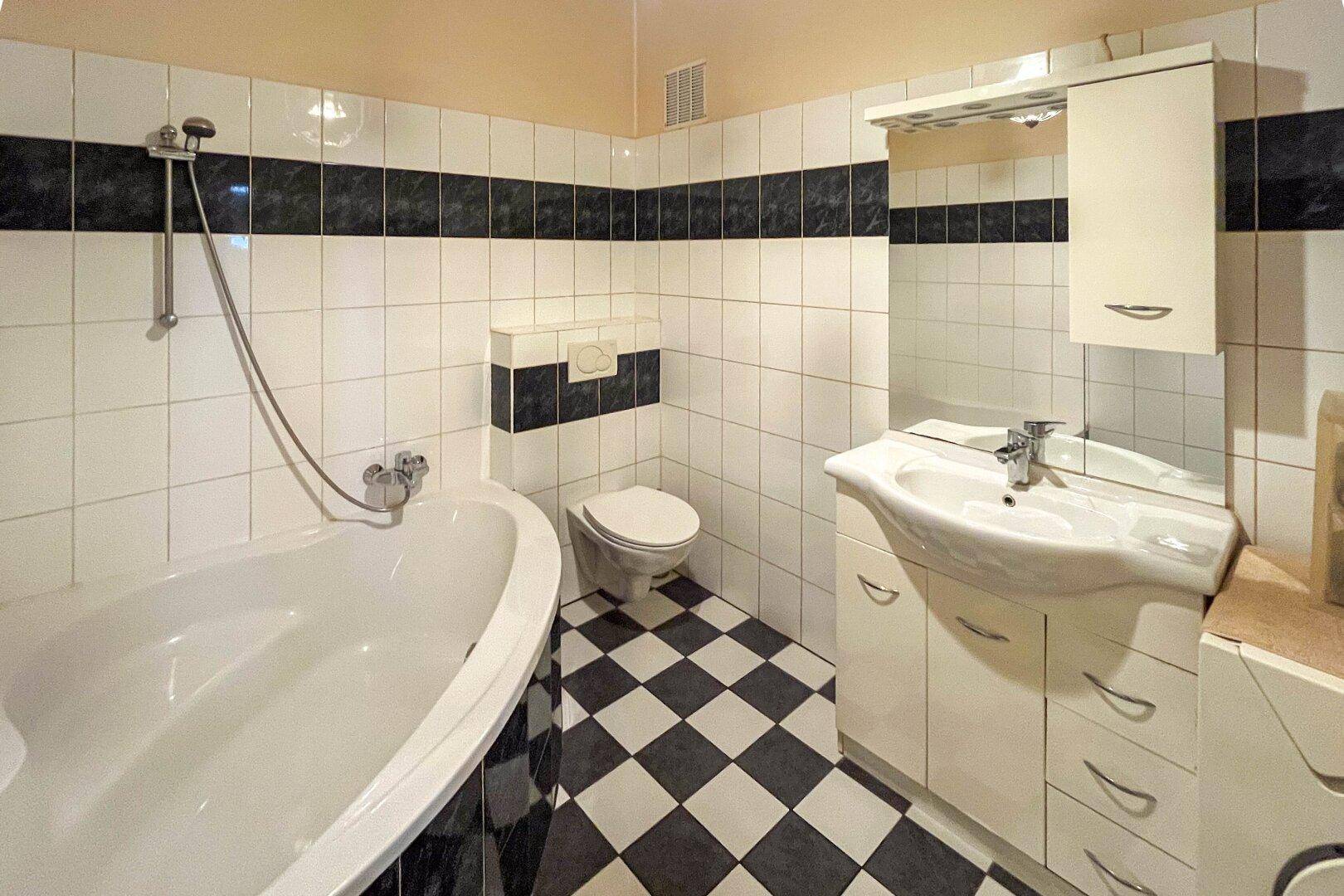 Badezimmer mit Badewanne, WC und Waschbecken, gefliest in Schwarz-Weiß-Muster.