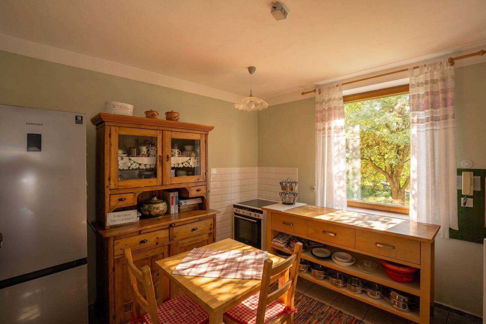 Gemütliche Küche mit Holzmöbeln, Esstisch und Fenster mit Blick ins Grüne.