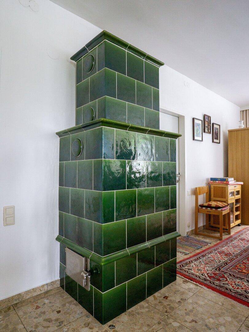 Traditioneller grüner Kachelofen als Heizelement in einem Wohnbereich mit Teppich.