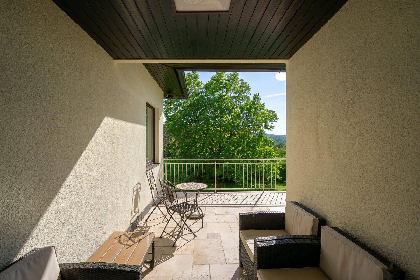 Überdachter Balkon mit Sitzgelegenheiten und weitem Blick über die grüne Landschaft.