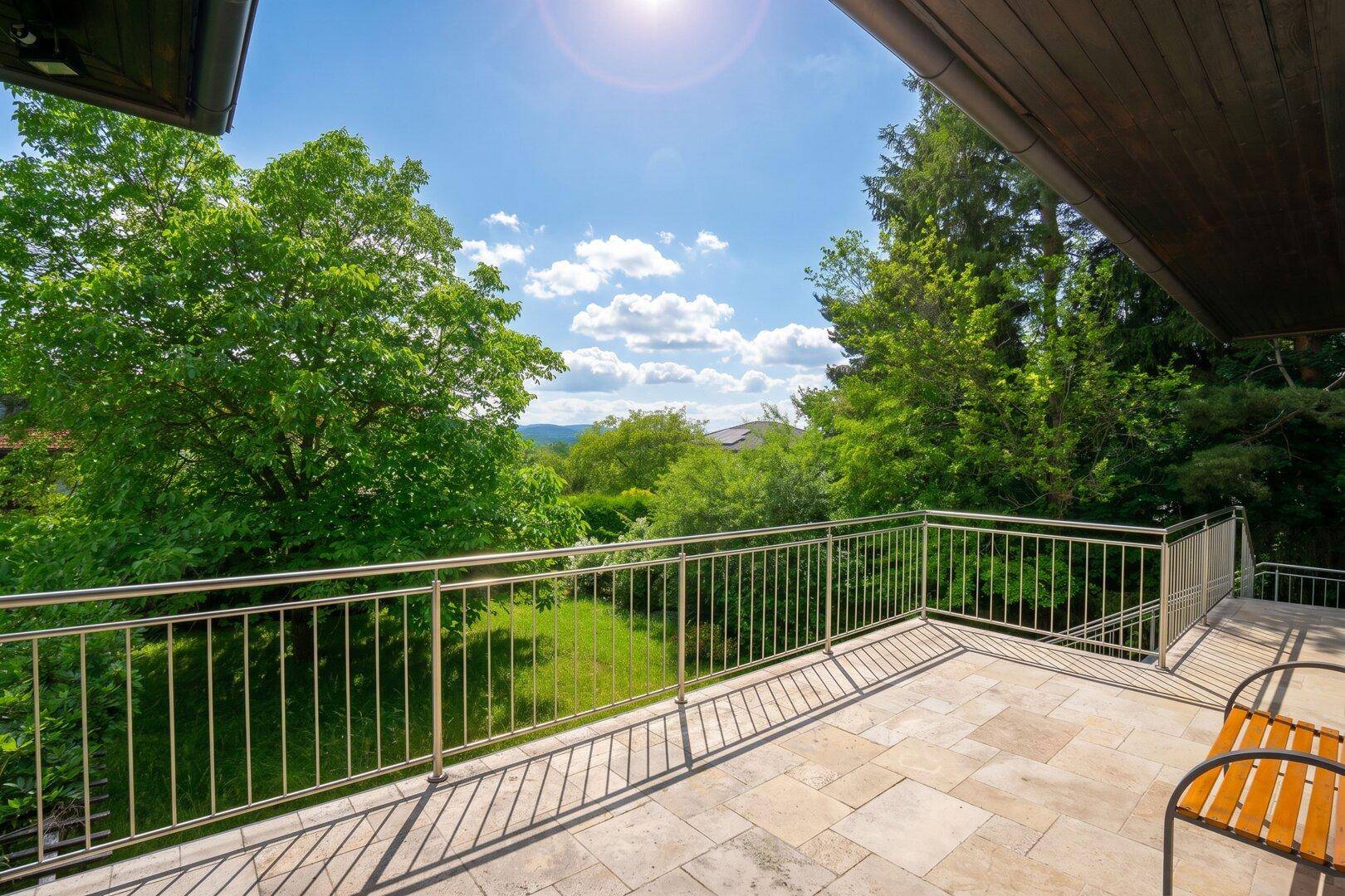 Großer offener Balkon mit Metallgeländer und sonnigem Ausblick auf die Natur.