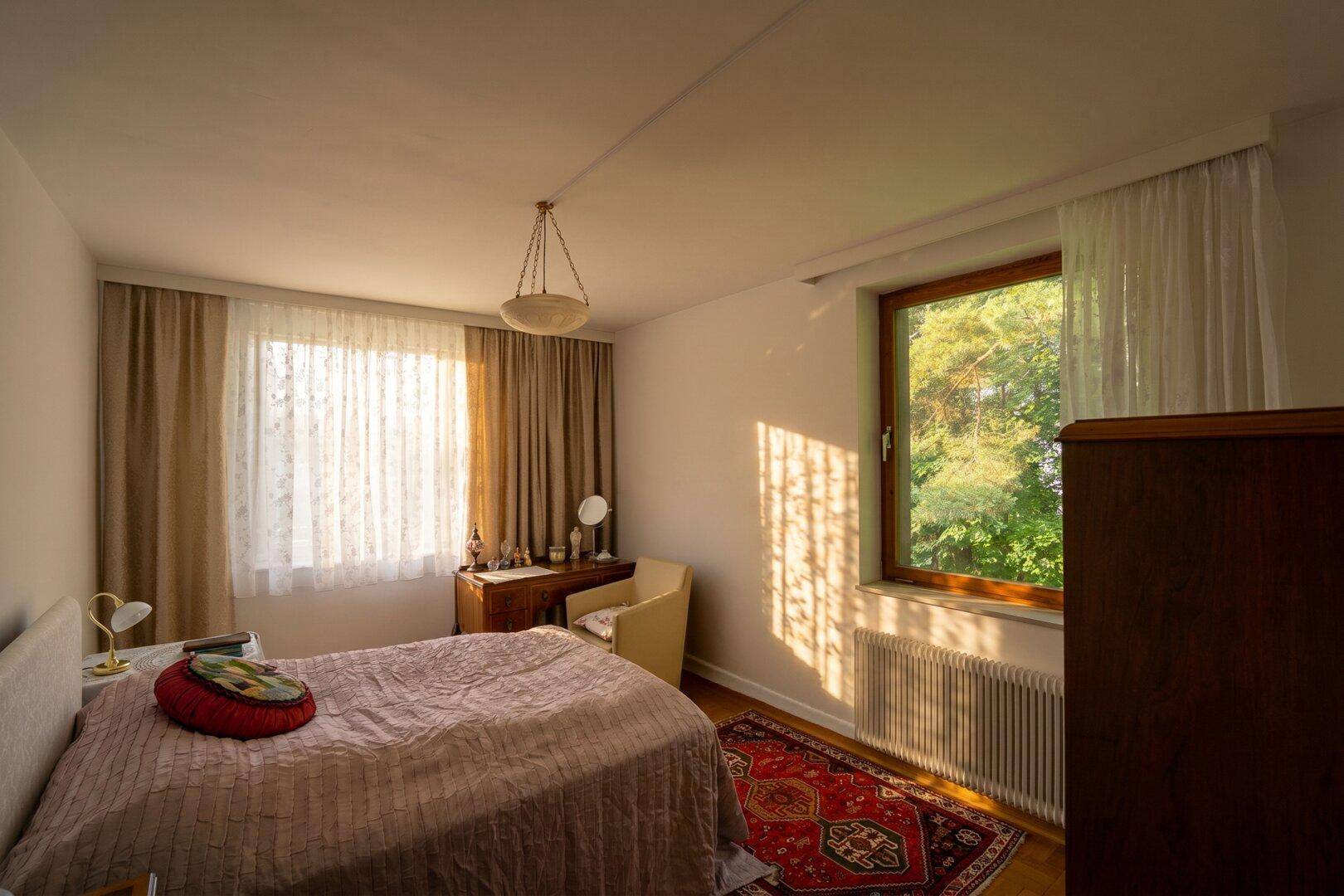 Helles Schlafzimmer mit Doppelbett, Holzmöbeln und Fenster mit viel Tageslicht.