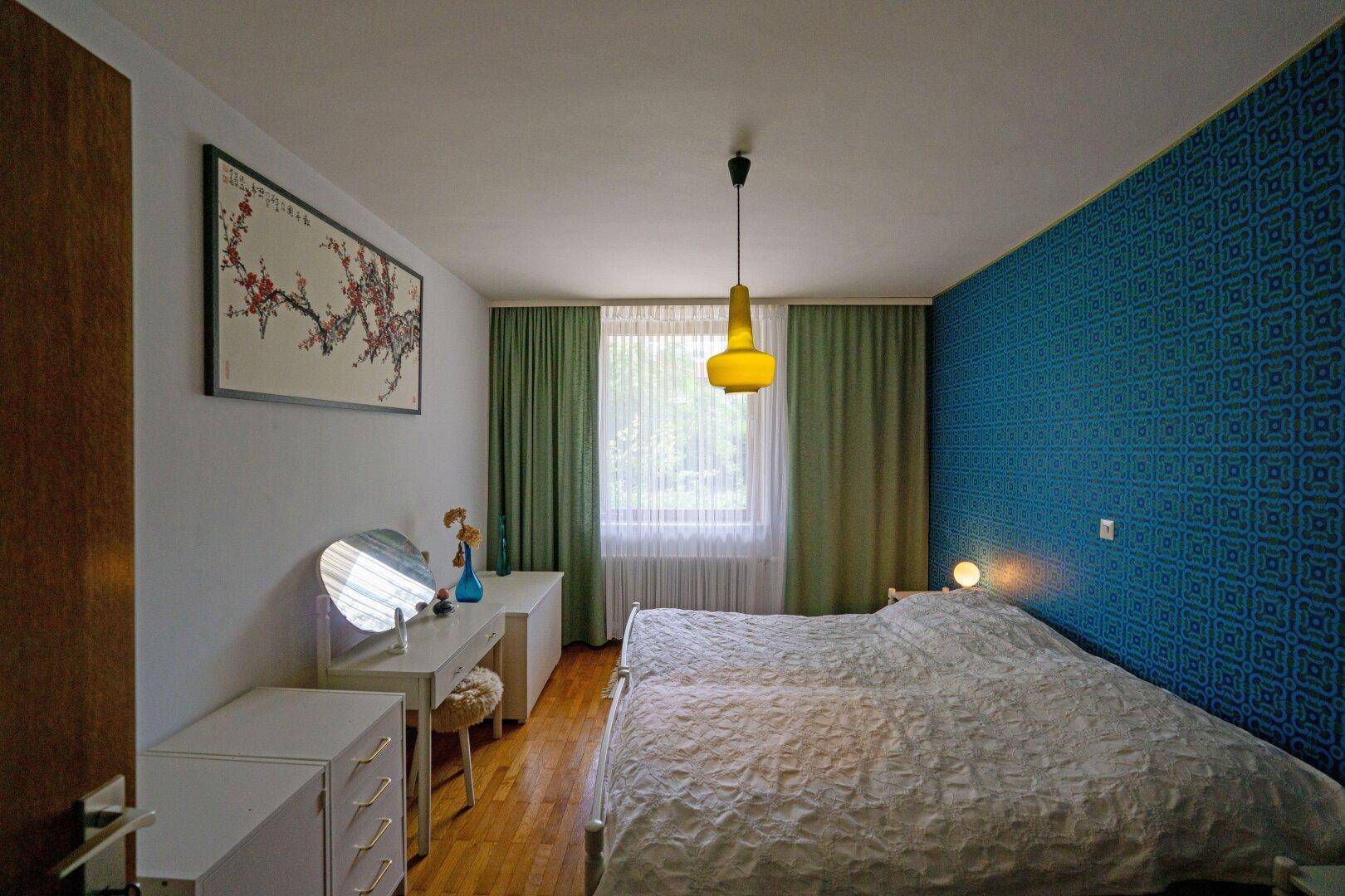 Schlafzimmer mit gemusterter Akzentwand, Doppelbett und Holzfußboden.