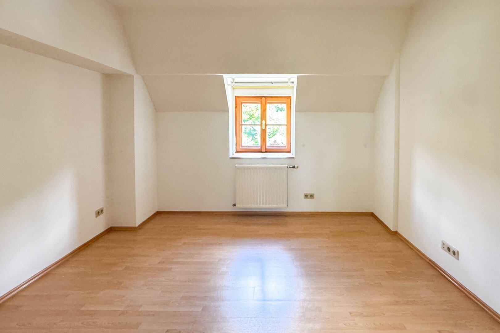 Geräumiges Zimmer mit Holzboden und schrägen Wänden, ideal als Schlaf- oder Arbeitszimmer nutzbar.