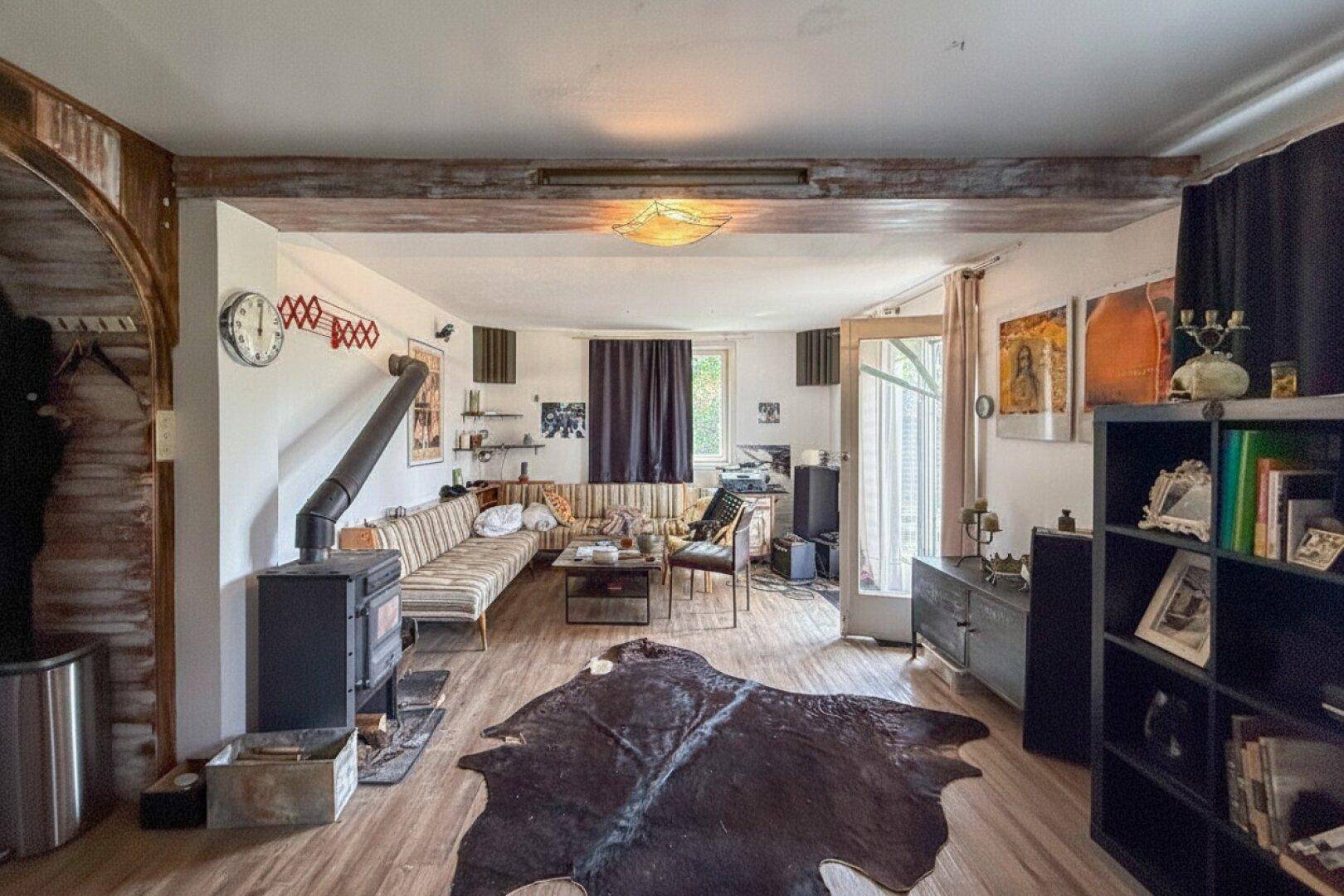 Rustikales Wohnzimmer mit Holzbalken, Kaminofen und gemütlicher Sitzecke.