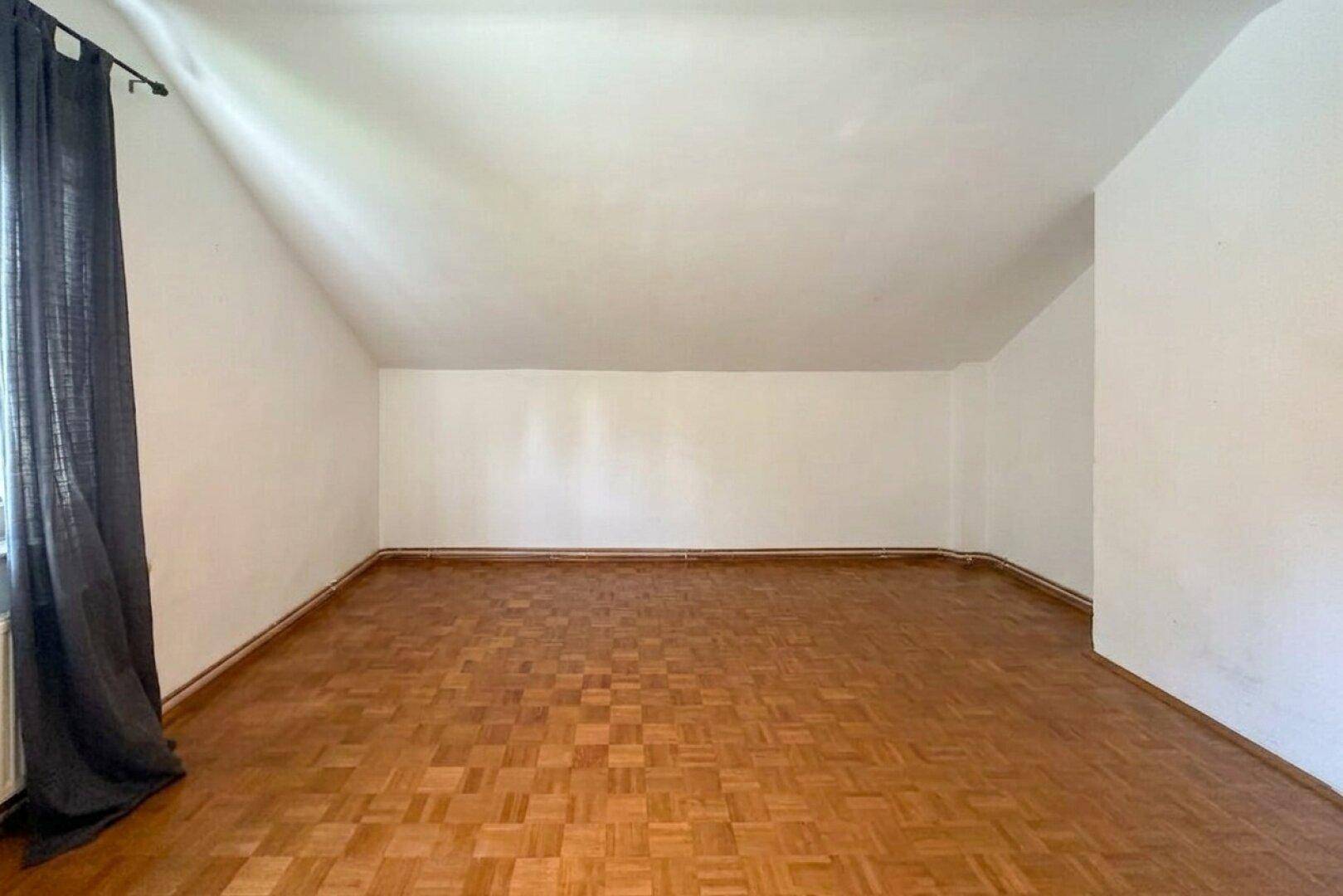Leeres Zimmer im Dachgeschoss mit Parkettboden und schrägen Wänden, bereit zur Einrichtung.