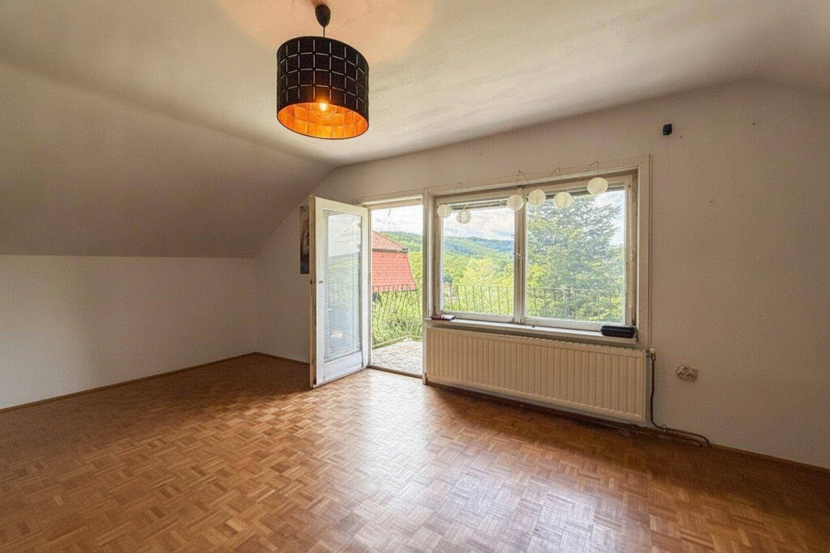 Helles Zimmer im Dachgeschoss mit Parkettboden, Balkonzugang und weitem Ausblick.