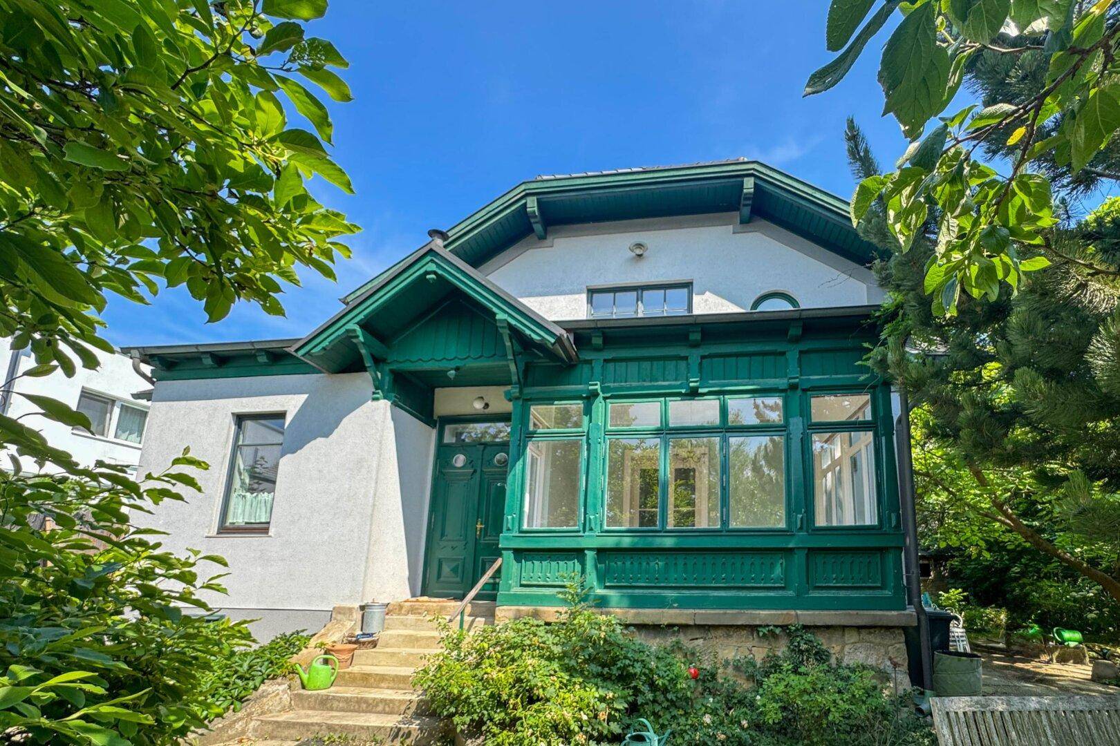 Vorderansicht des Hauses mit markanter grüner Veranda und großen Fenstern.