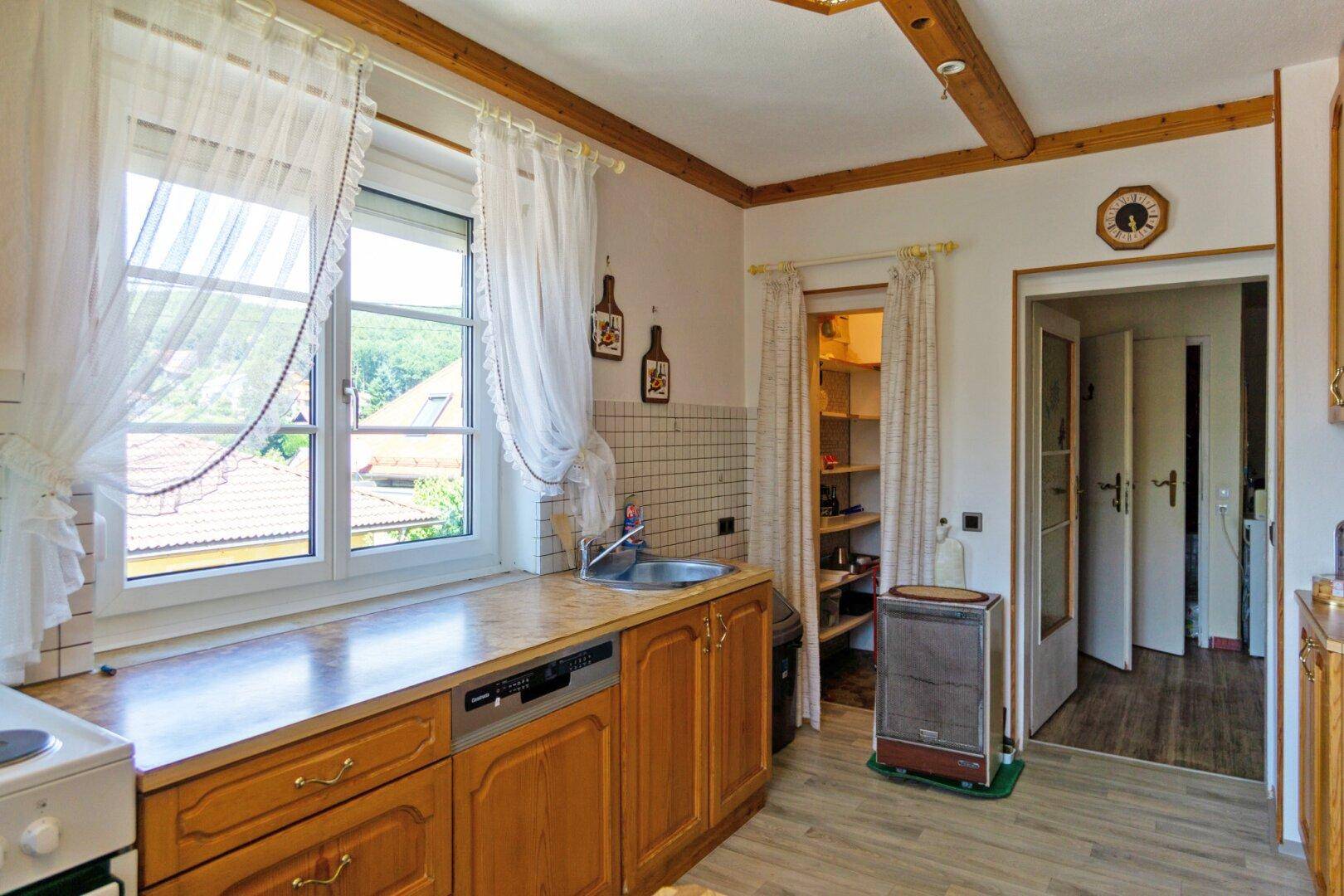 Gemütliche Küche mit Holzschränken, Spülbecken und Zugang zu einer praktischen Speisekammer.