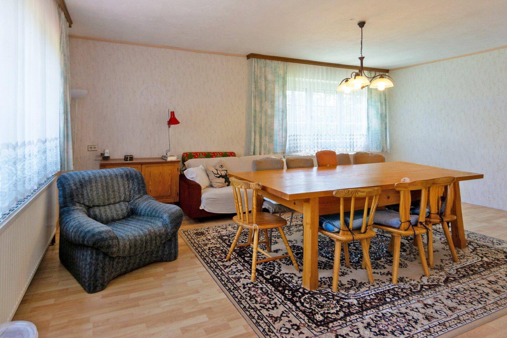 Geräumiger Wohn-Essbereich mit großem Holztisch, Teppich und bequemen Sitzgelegenheiten.
