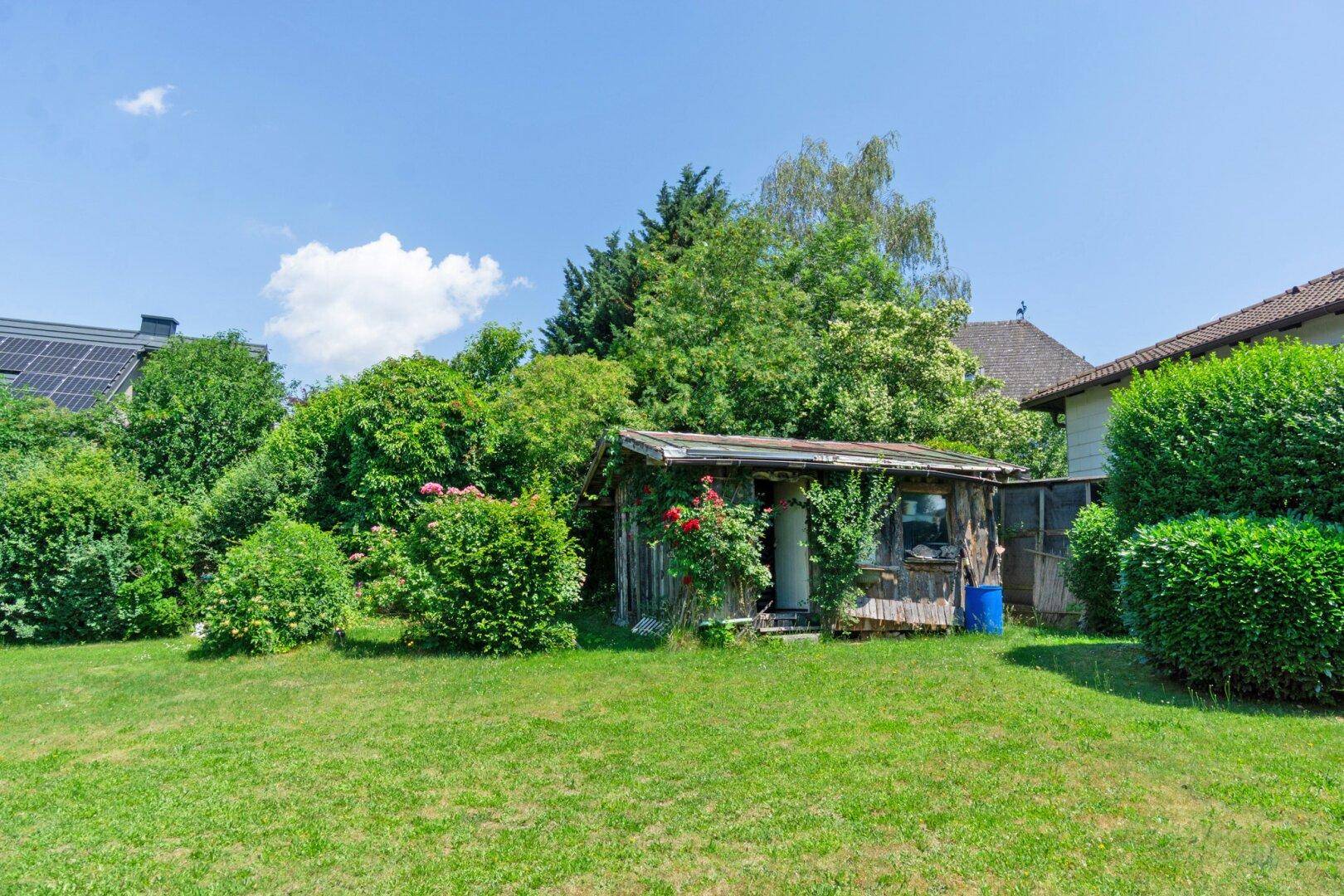 Großer, gepflegter Garten mit Rasenfläche, Sträuchern und einem kleinen Gartenhaus.
