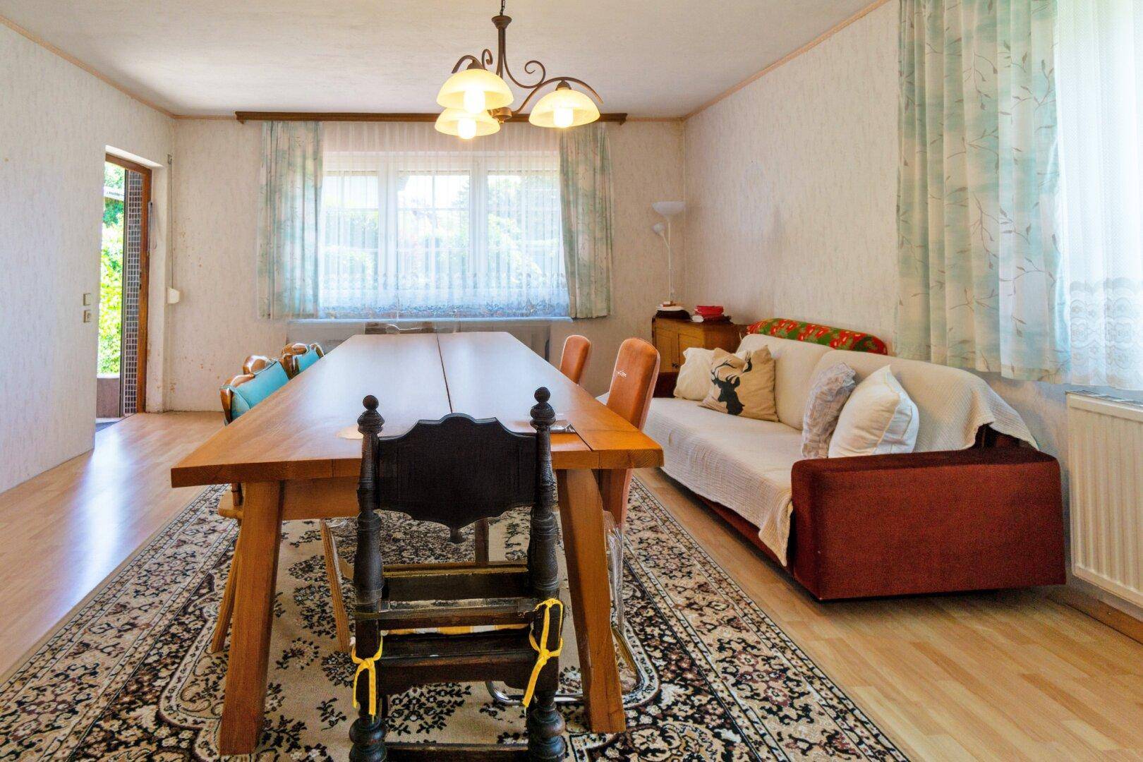 Heller Wohn-Essbereich mit großem Esstisch, Sofa und Blick durch das Fenster.