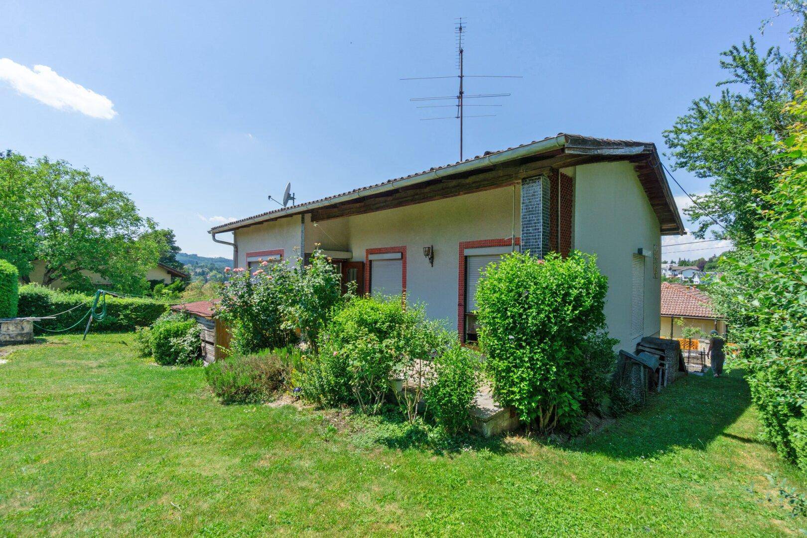 Rückseite des Hauses mit Gartenbereich, grünen Büschen und Blick in die Ferne.