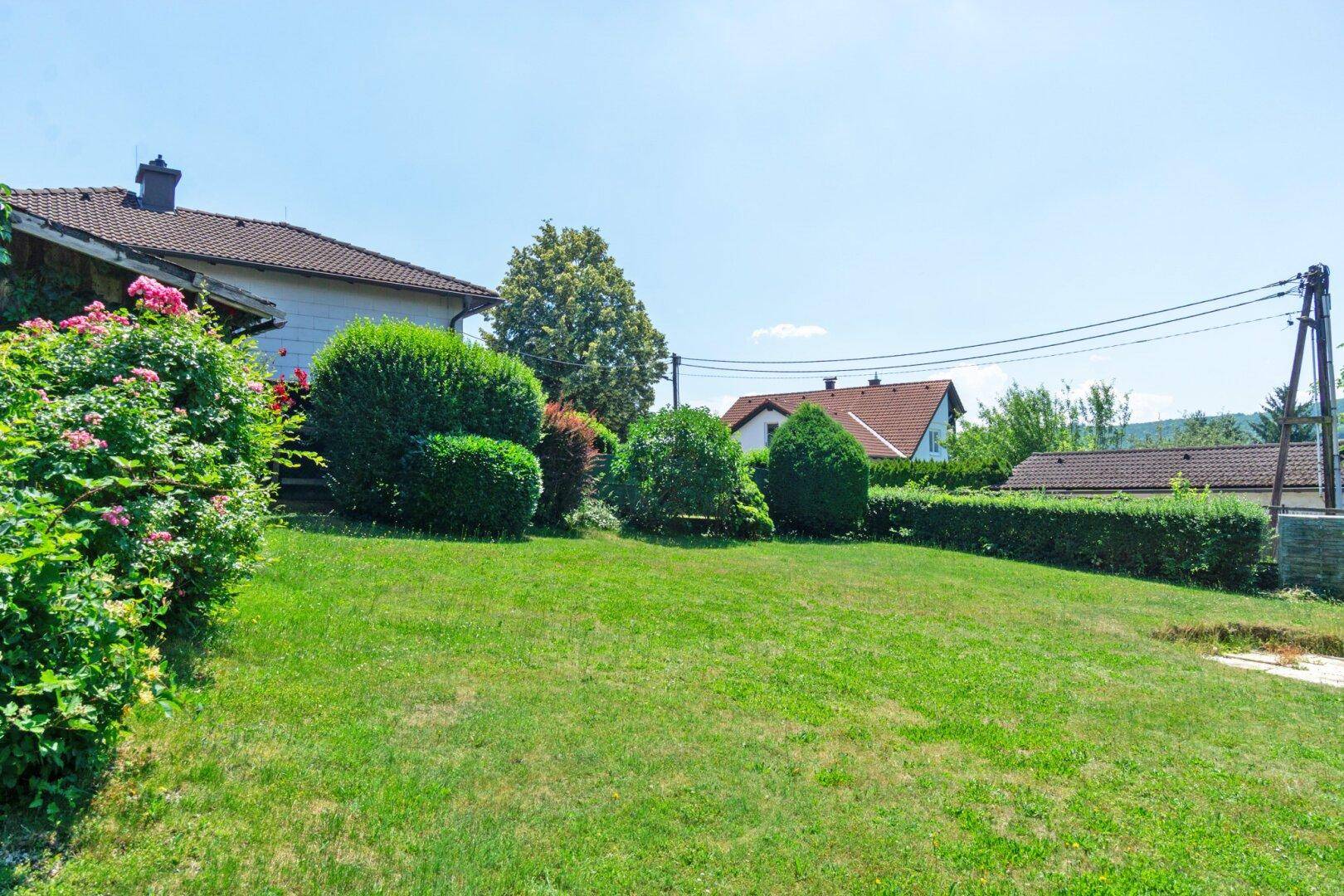 Weitläufiger Garten mit Rasenfläche, Hecken und Blick auf die umliegende Landschaft.