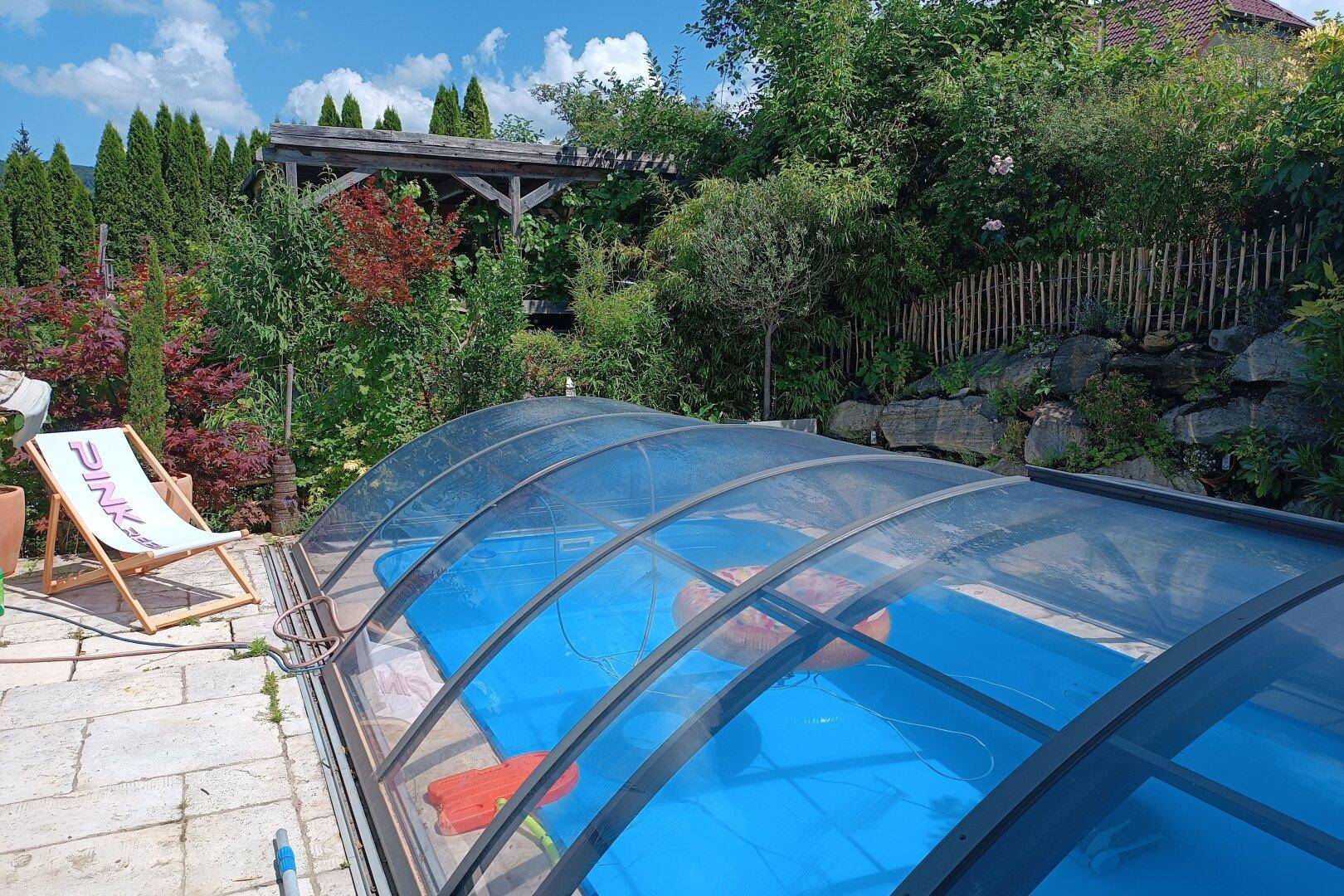 Überdachter Poolbereich im Garten mit Liegestuhl und Steinplattenboden.