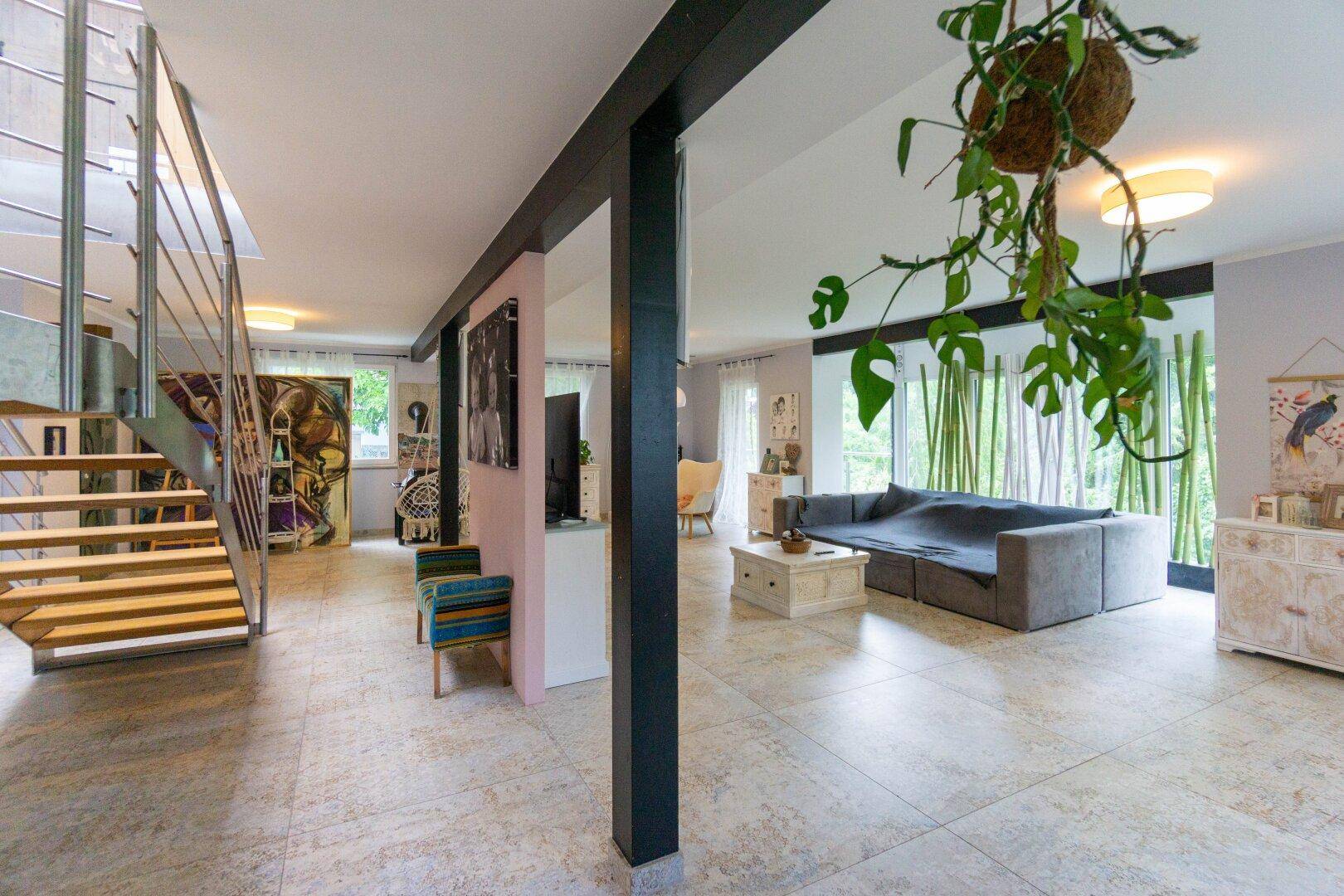 Geräumiges Wohnzimmer mit großem Sofa, Fliesenboden und Blick ins Grüne.