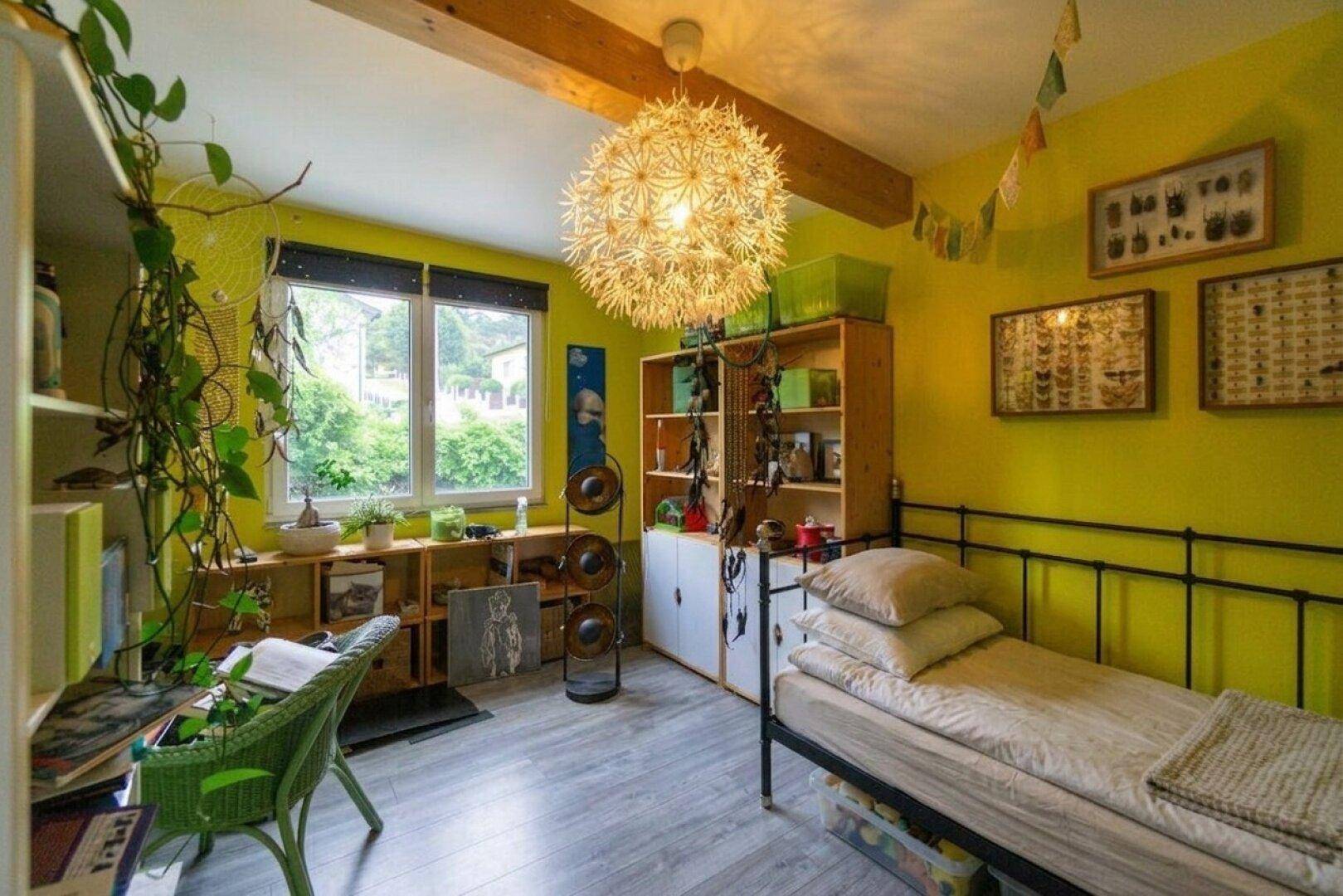 Farbenfrohes Schlafzimmer mit Einzelbett, Holzbalken und Blick in den Garten.