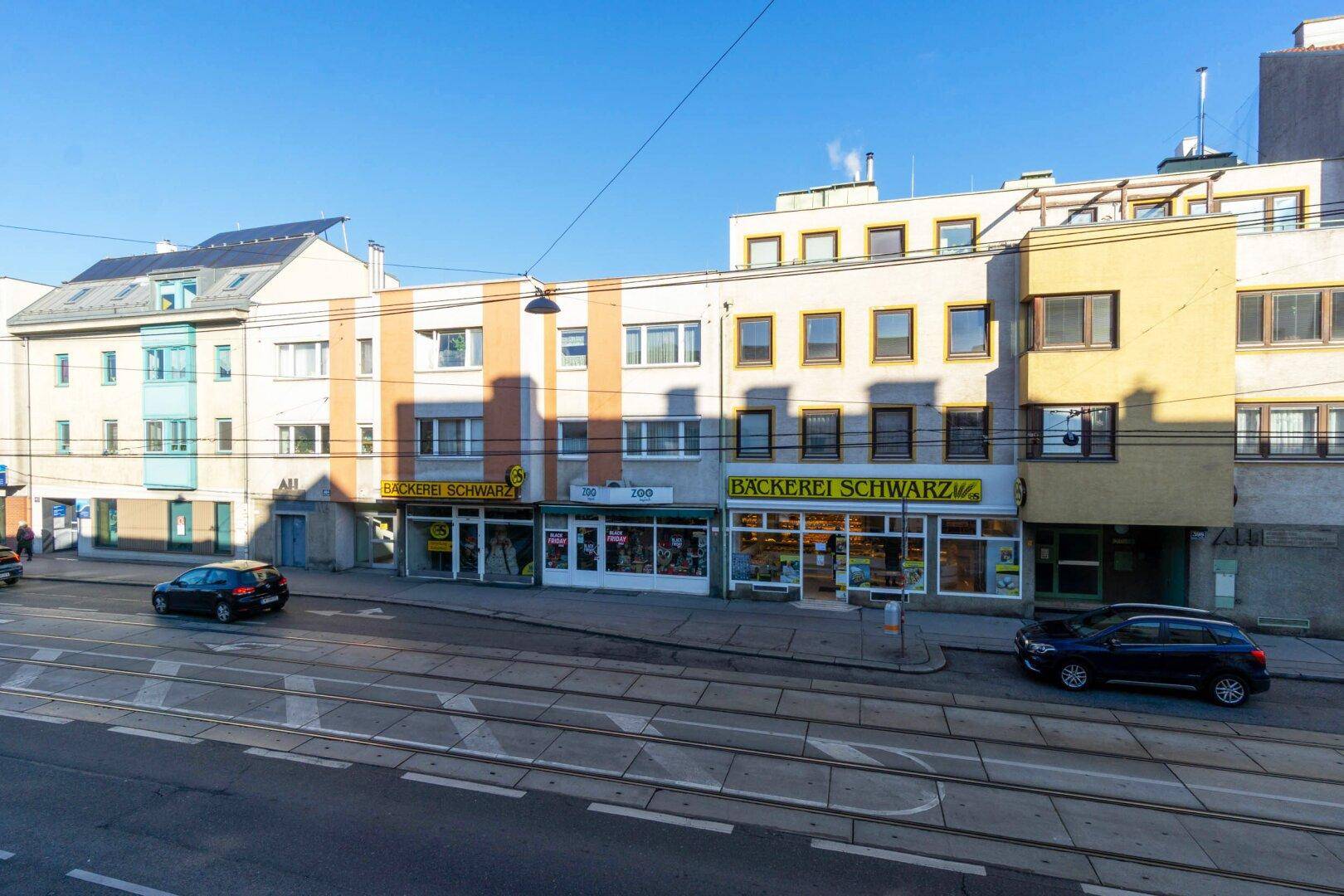 Reihe von Gebäuden entlang einer Straße mit Geschäften im Erdgeschoss und Wohnungen darüber unter blauem Himmel.