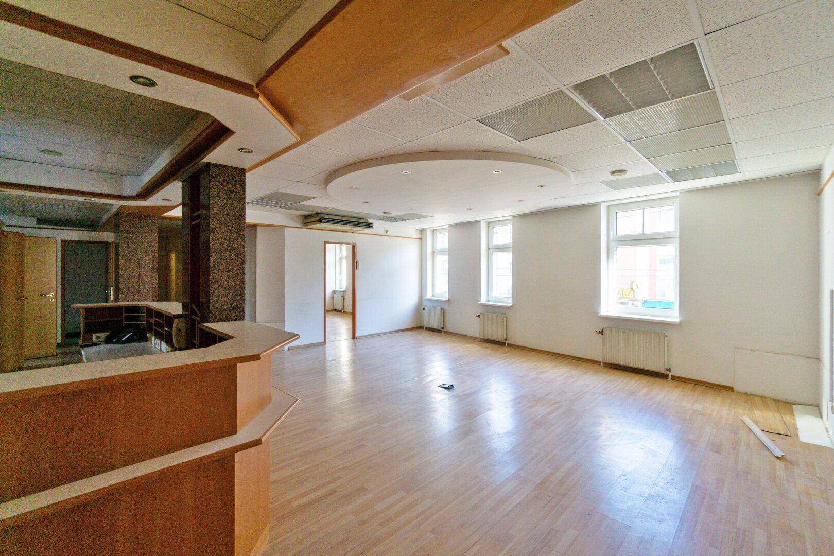 Weitläufiger Gewerberaum mit Holzfußboden, Theke und mehreren Fenstern, bietet vielseitige Nutzungsmöglichkeiten.