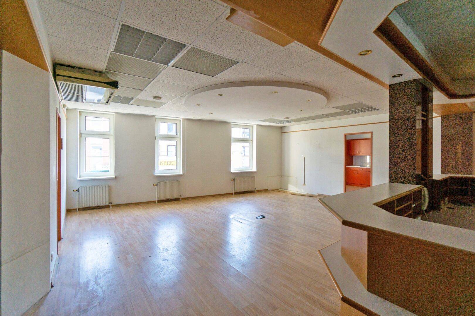 Großer, leerer Gewerberaum mit Thekenbereich, Holzfußboden und abgehängter Decke, ideal für verschiedene Nutzungen.