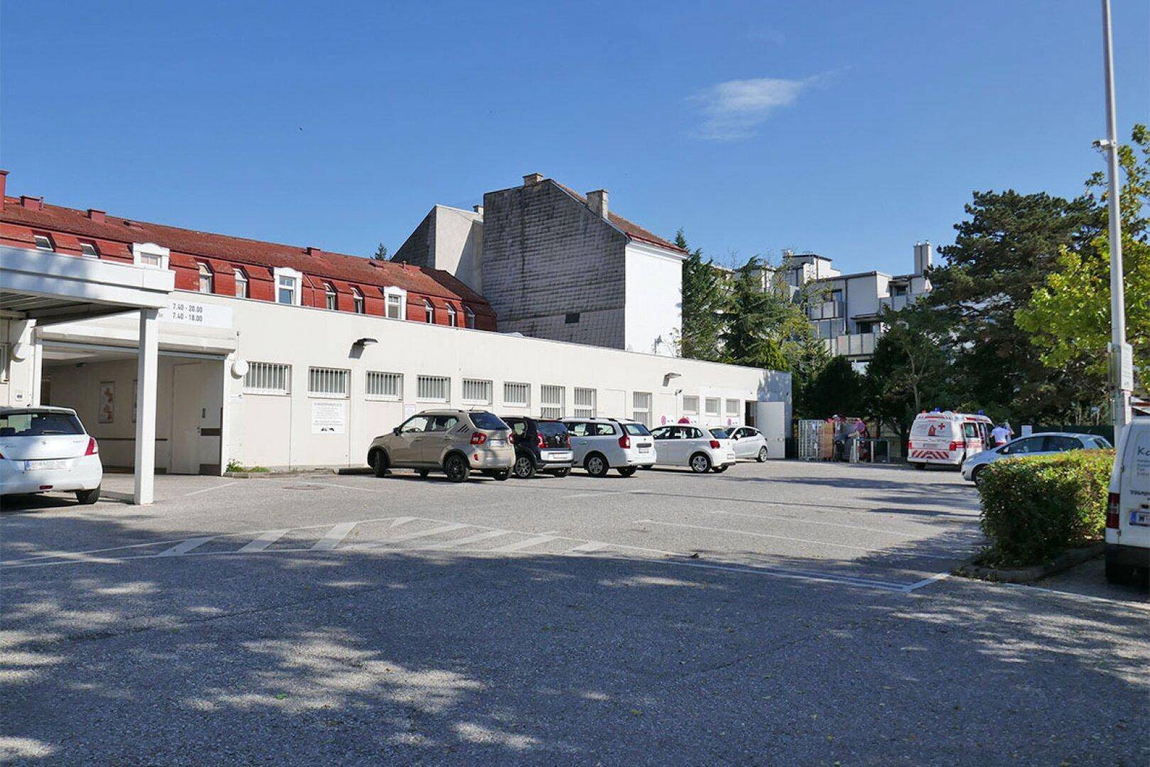 Großer Parkplatz mit mehreren Autos und einem Gebäude im Hintergrund unter klarem blauem Himmel.