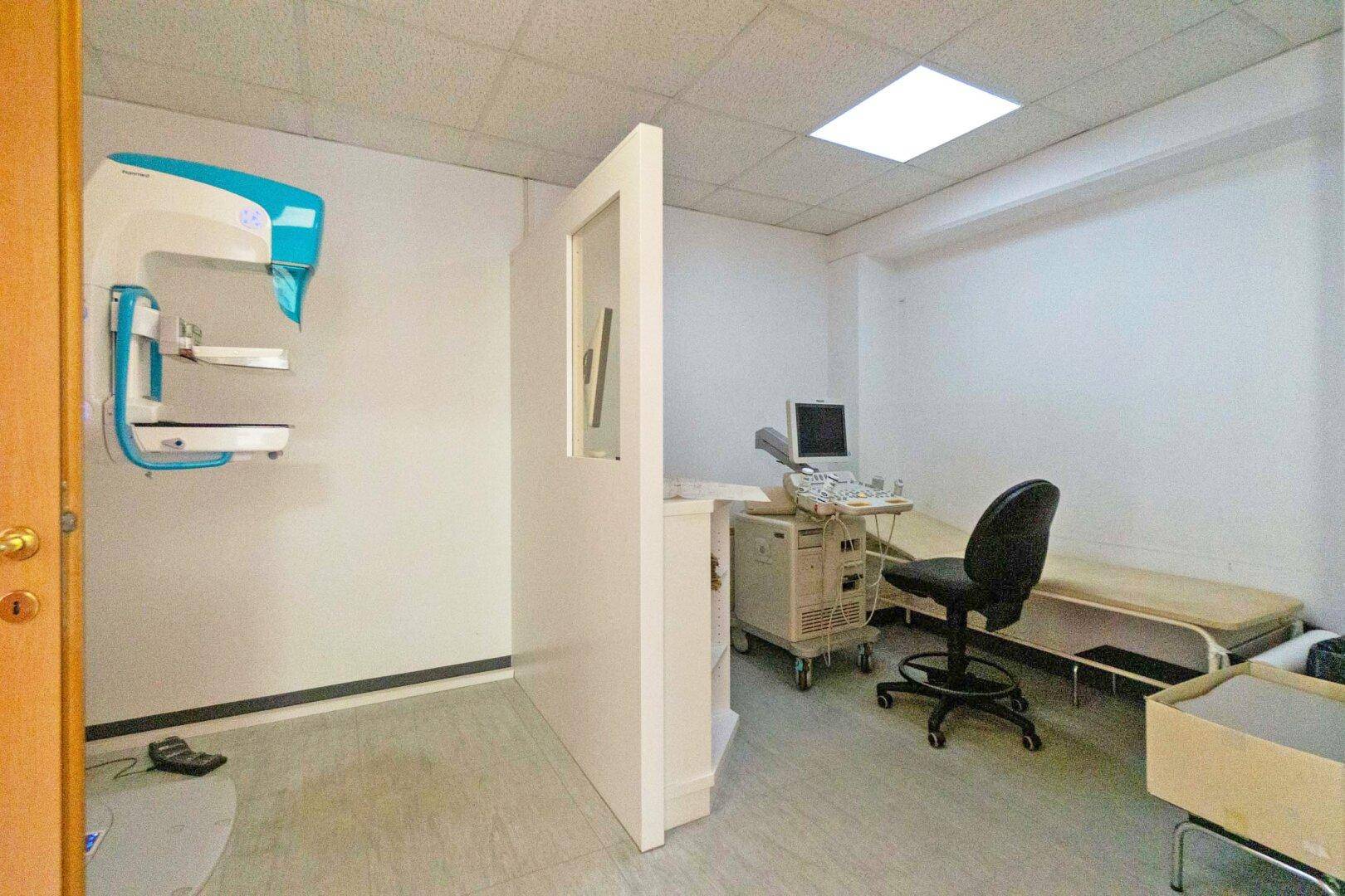 Untersuchungsraum mit Mammographiegerät, Liege und einem Computerarbeitsplatz für Diagnosen.