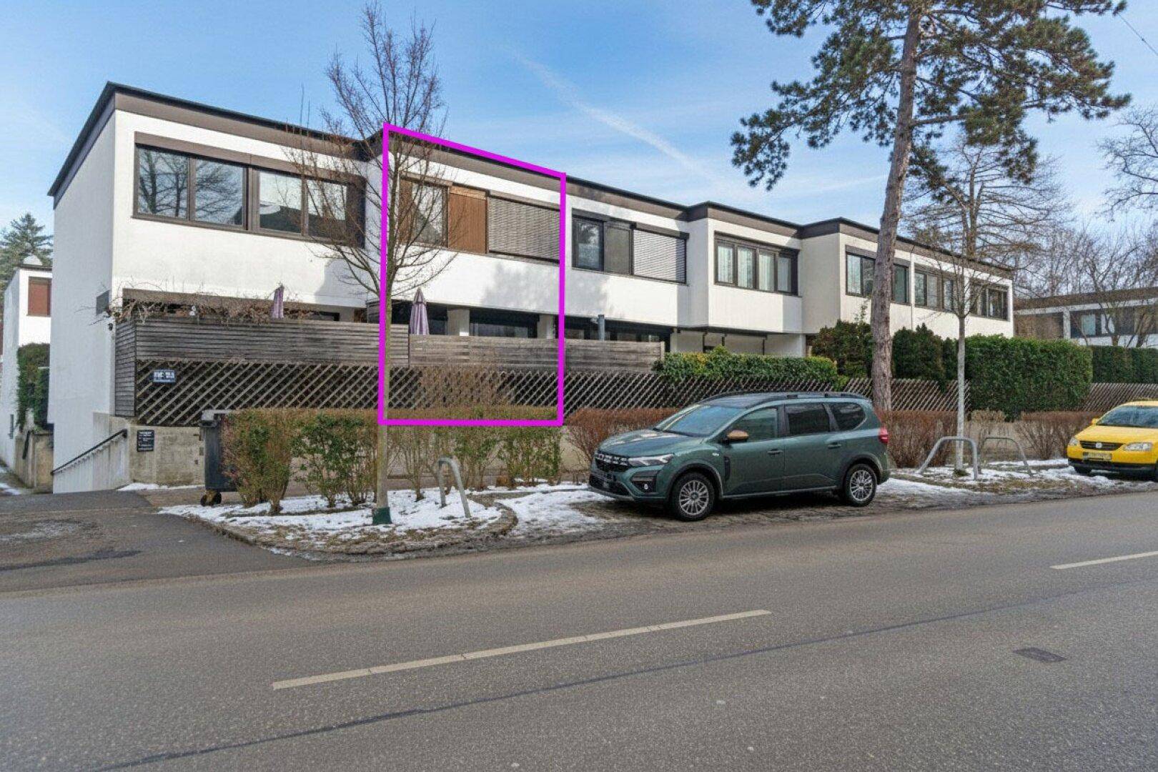 Außenansicht eines modernen Reihenhauses mit mehreren Wohneinheiten und Vorgarten an einer Straße.