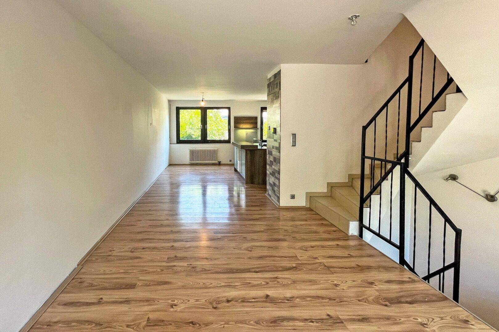 Offener Wohnbereich mit Laminatboden und Treppe, der in eine moderne Küche übergeht.