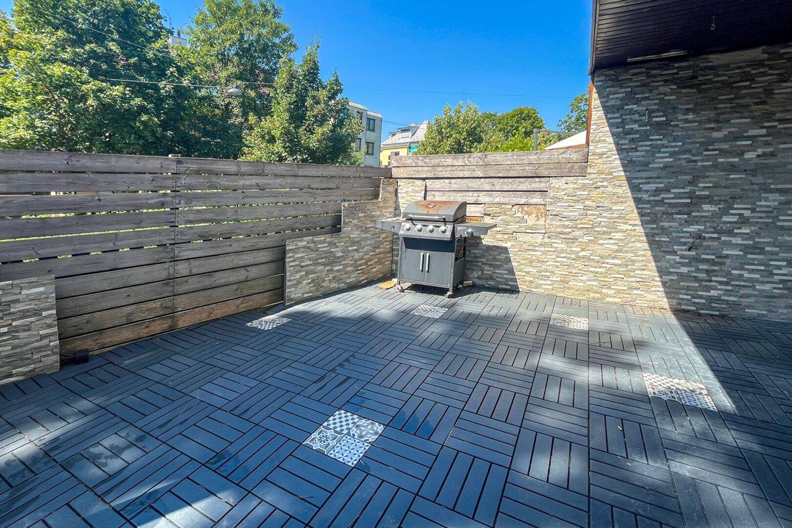 Geräumige Terrasse mit Grillbereich, dunklen Fliesen und einer Kombination aus Holz- und Steinwänden.