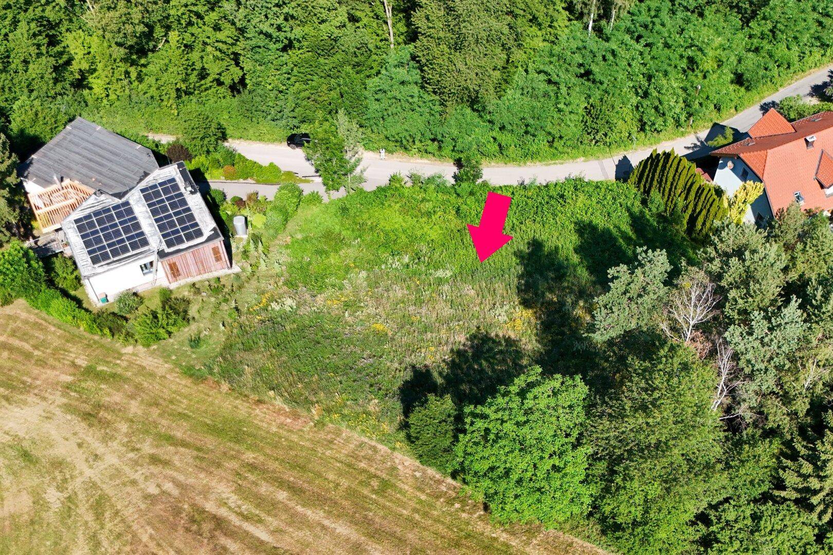 Luftaufnahme eines Baugrundstücks, umgeben von üppiger Vegetation und landwirtschaftlichen Flächen.