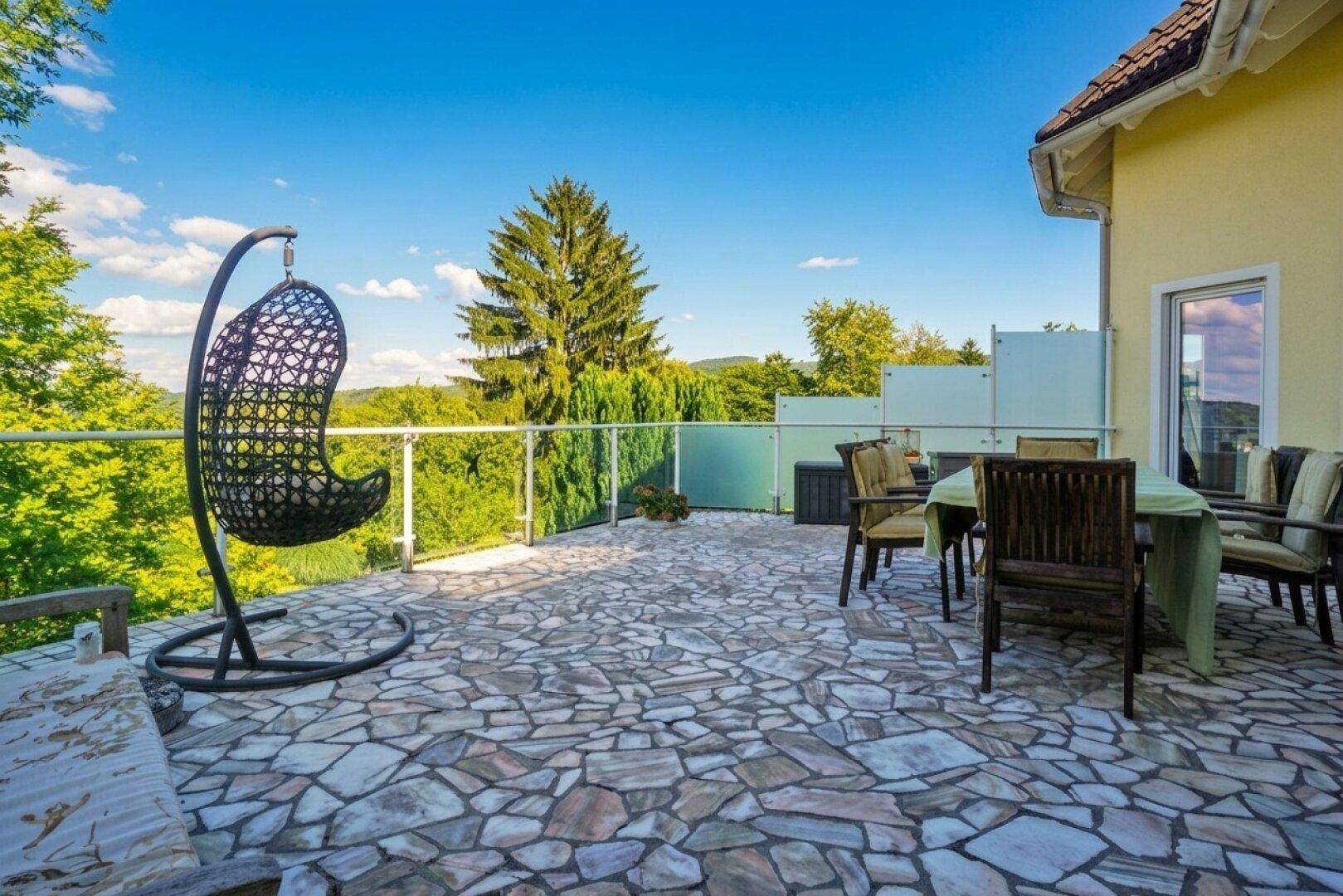 Große, gepflasterte Terrasse mit Sitzgelegenheiten und weitem Blick über die grüne Landschaft.