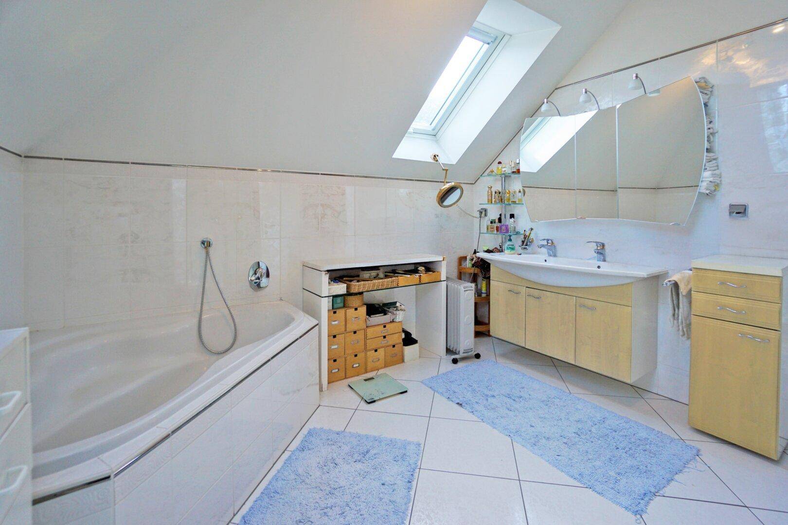 Helles Badezimmer mit Badewanne, Fliesenboden und Dachfenster für natürliches Licht.