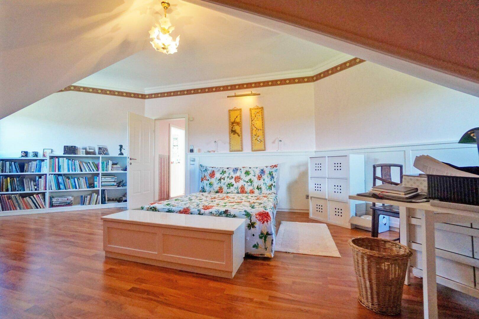Gemütliches Schlafzimmer mit Holzboden, integrierten Bücherregalen und schrägen Decken.