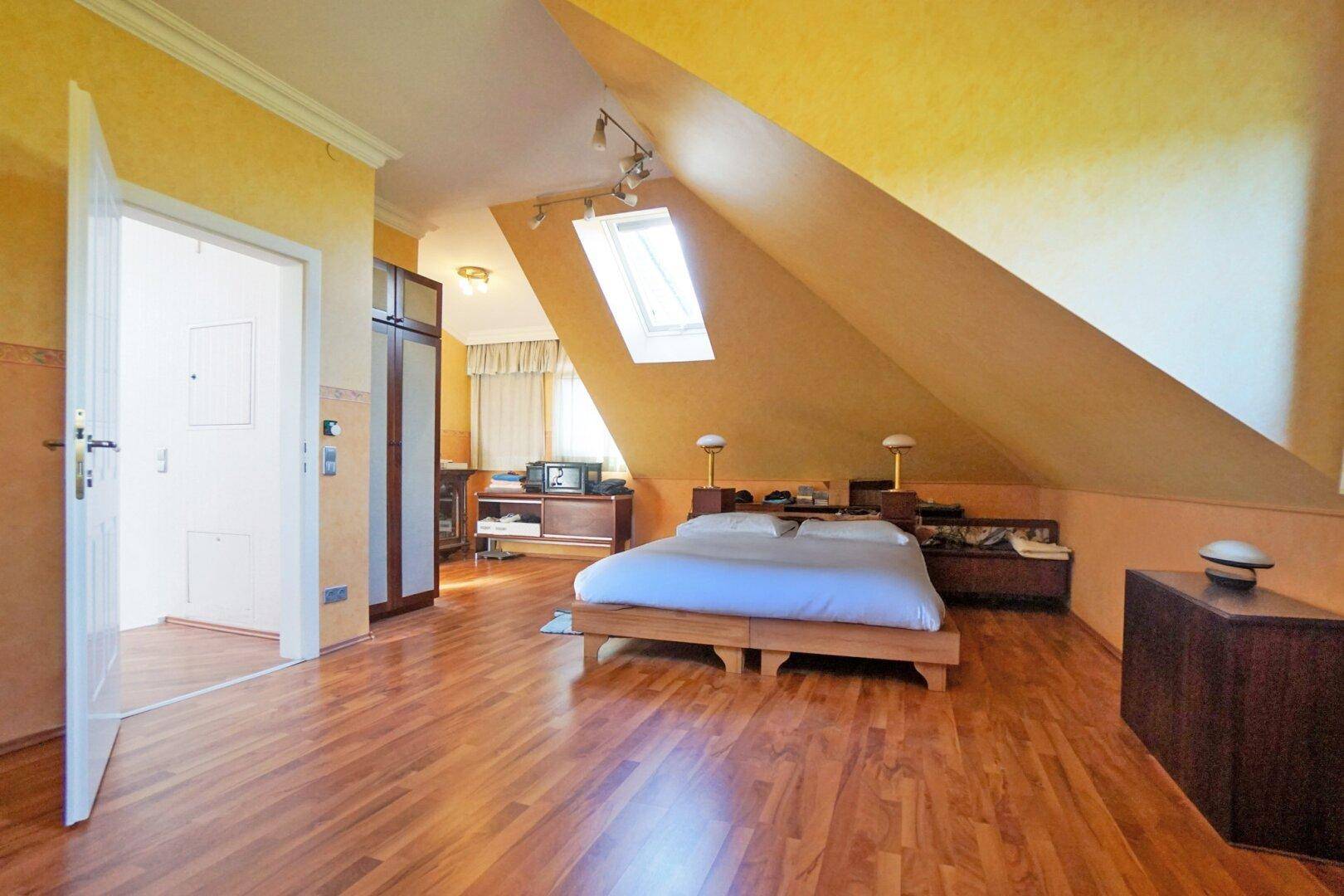 Geräumiges Schlafzimmer mit Holzboden, Dachschrägen und einem Dachfenster für Helligkeit.