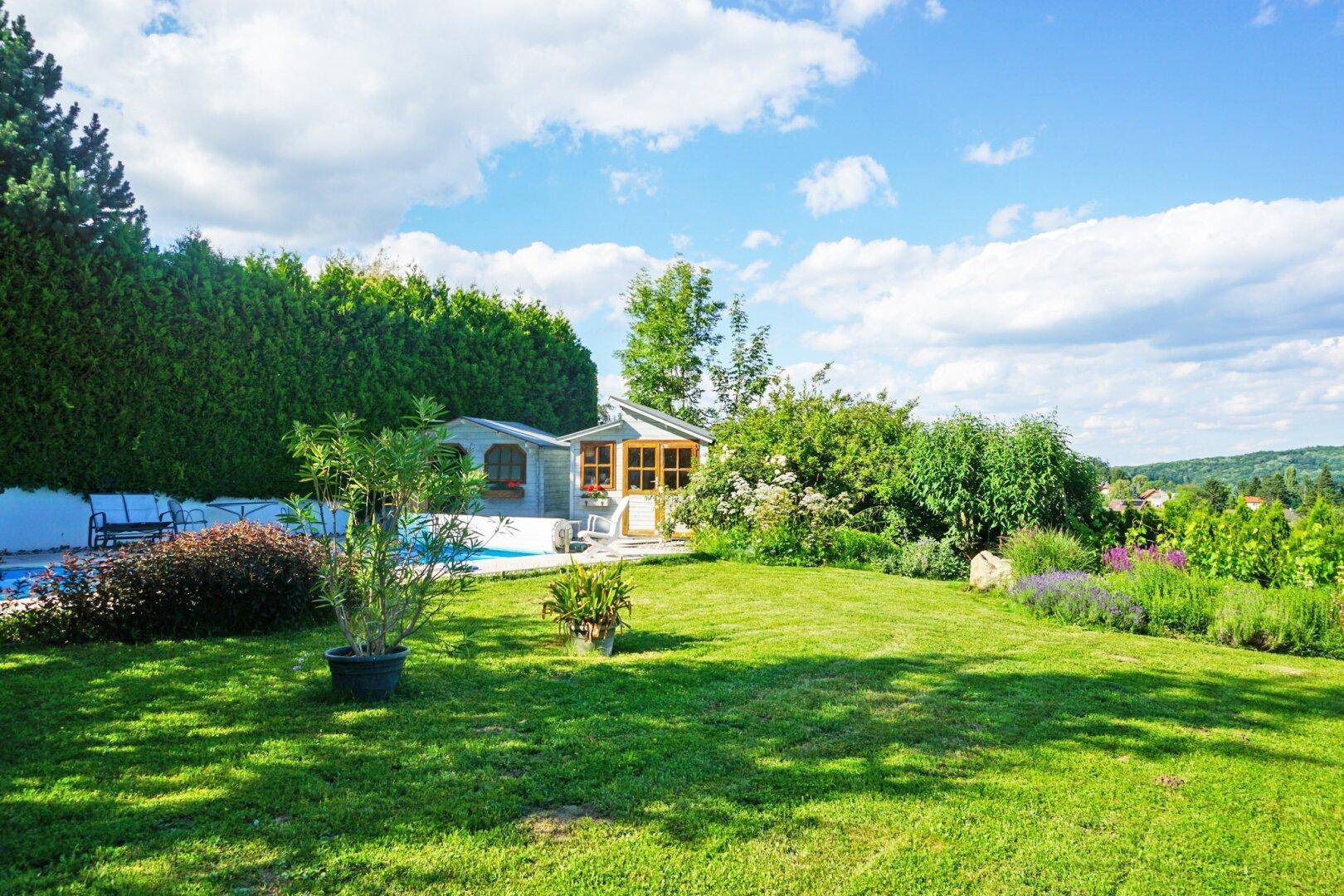 Gepflegter Gartenbereich mit Rasenfläche, Hecke und einem charmanten Poolhaus im Hintergrund.