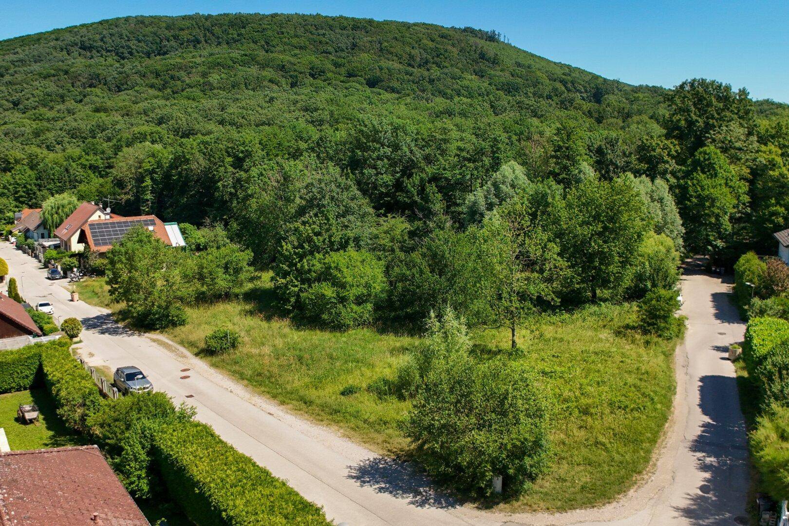 Weitläufige Luftaufnahme eines unbebauten Grundstücks mit angrenzenden Straßen und bewaldeten Hügeln im Hintergrund.