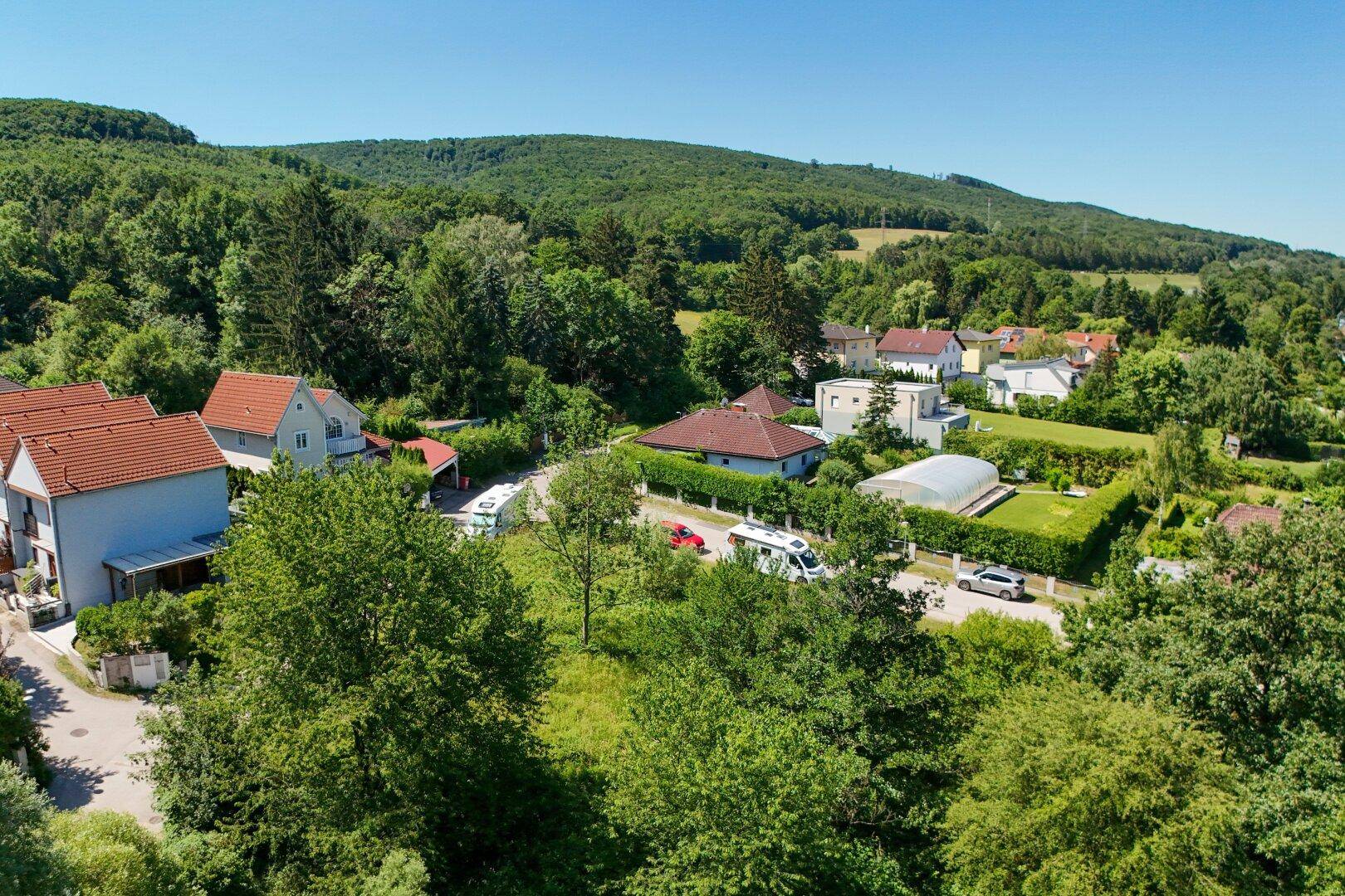 Überblick über eine ländliche Wohngegend mit Einfamilienhäusern, viel Grün und einem Gewächshaus im Gartenbereich.