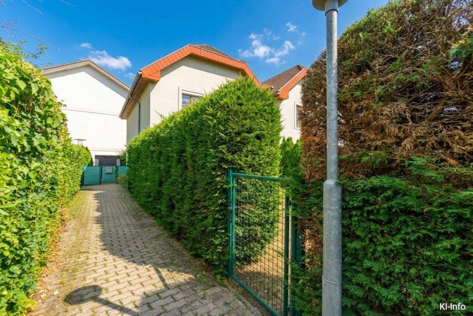 Gepflasterter Zugangsweg zum Haus, gesäumt von hohen, dichten Hecken für Privatsphäre.