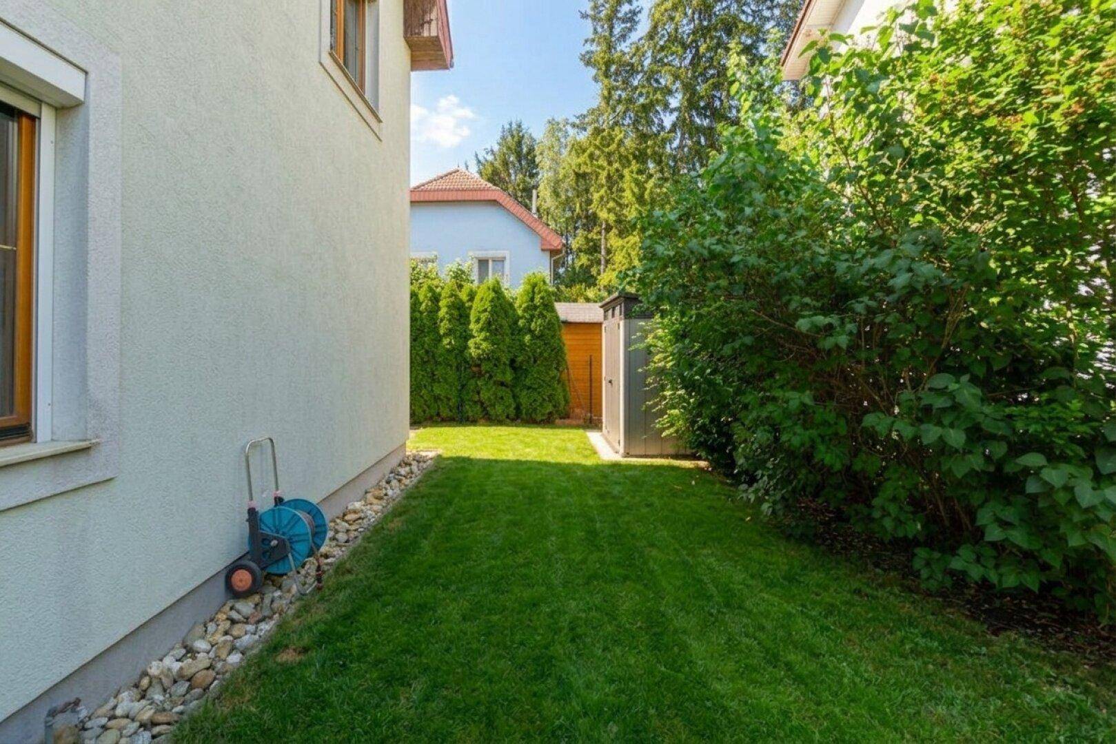 Seitlicher Gartenbereich mit Rasenfläche, Kiesstreifen und einem kleinen Gartenschuppen.