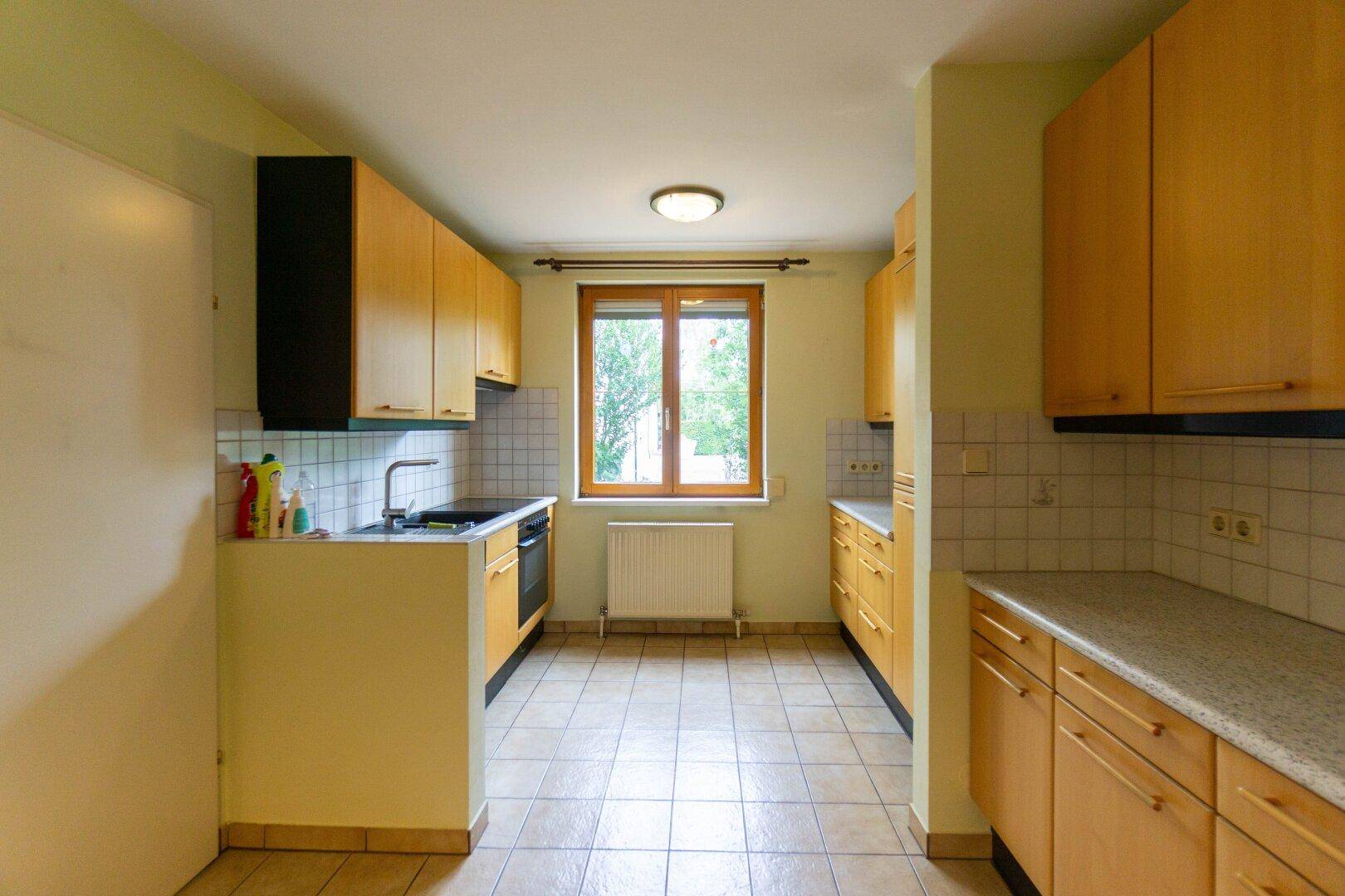 Funktionale Küche mit Holzschränken, Fenster und Fliesenboden, bereit zur individuellen Gestaltung.