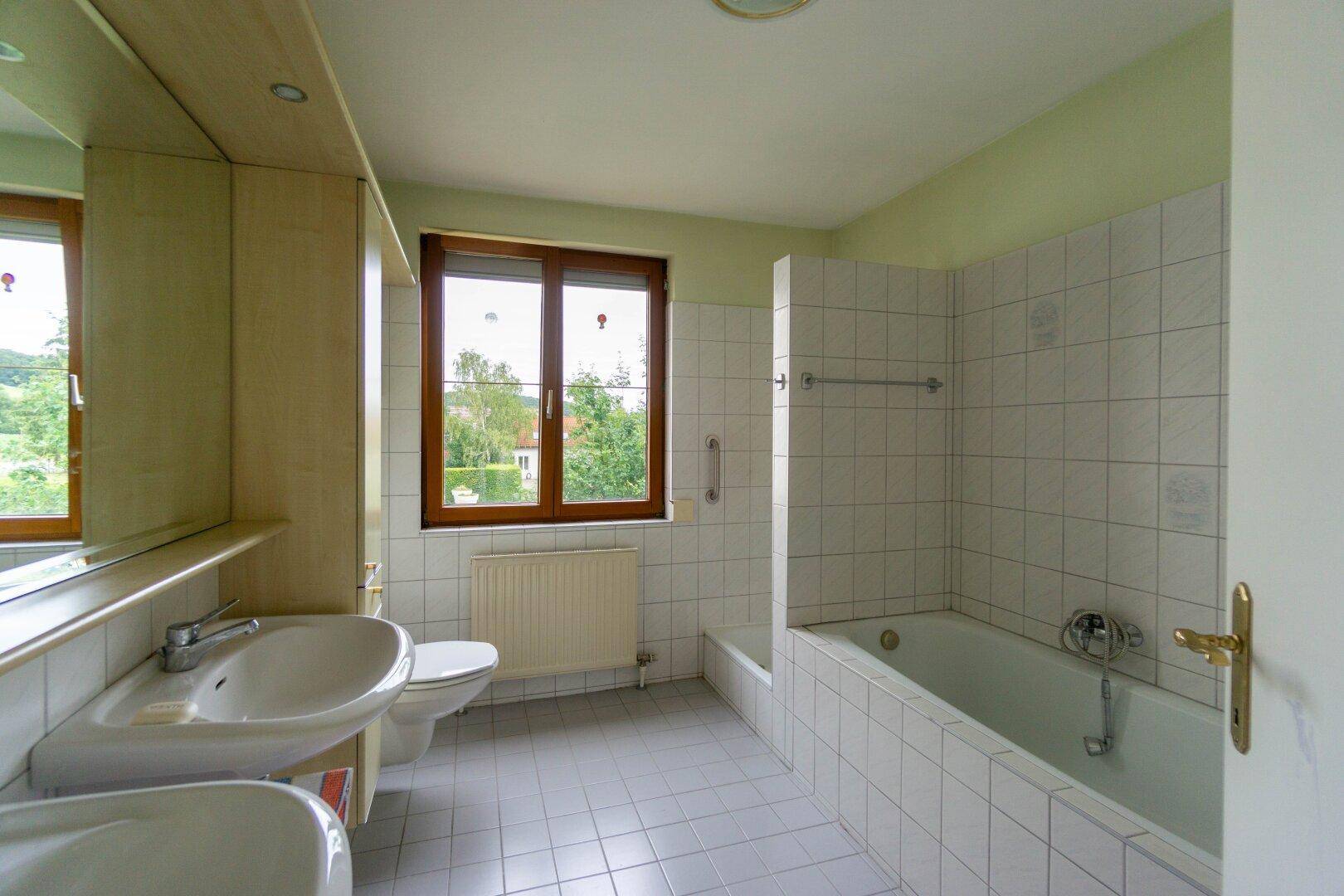 Badezimmer mit Badewanne, Doppelwaschbecken und Fenster, in einem gepflegten Zustand.