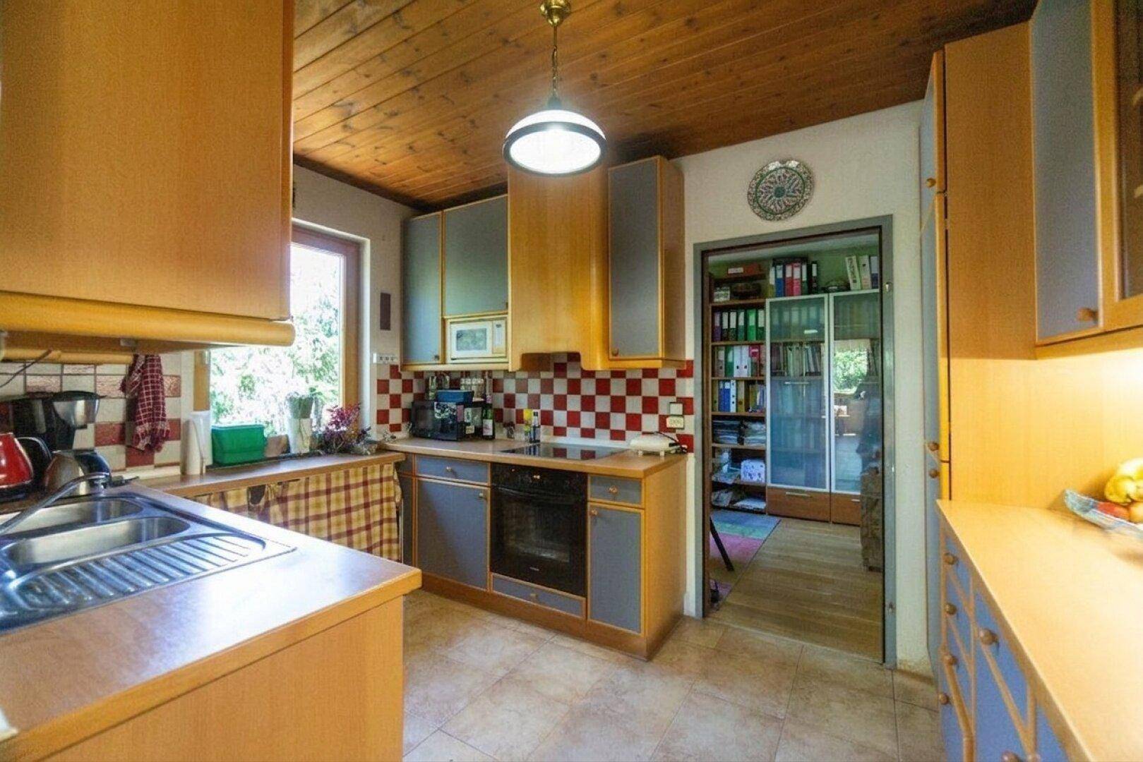 Funktionale Küche mit Holzschränken, gefliestem Boden und Durchgang zu einem weiteren Raum.