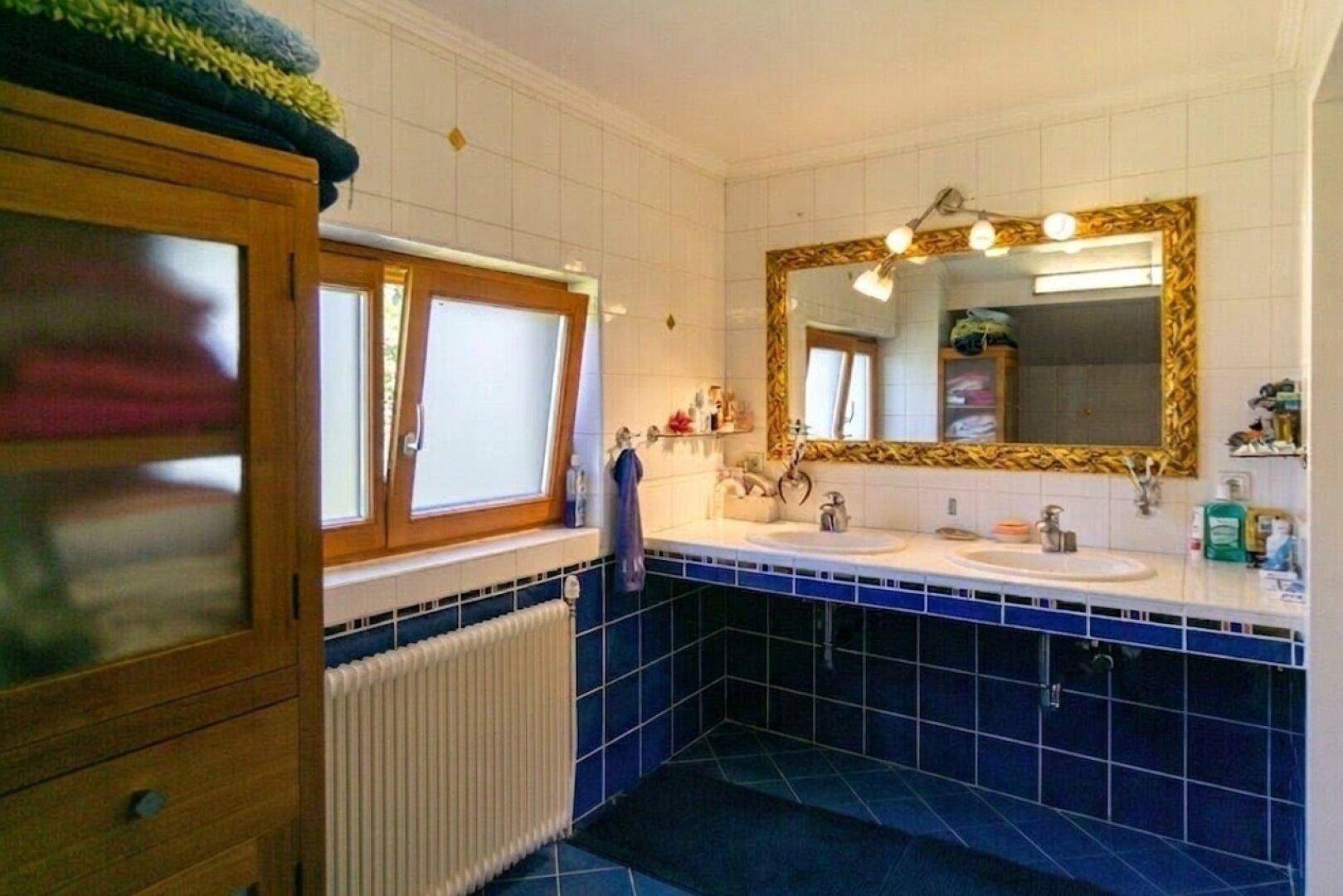 Badezimmer mit blauen und weißen Fliesen, Doppelwaschbecken und großem Spiegel, inklusive Fenster.