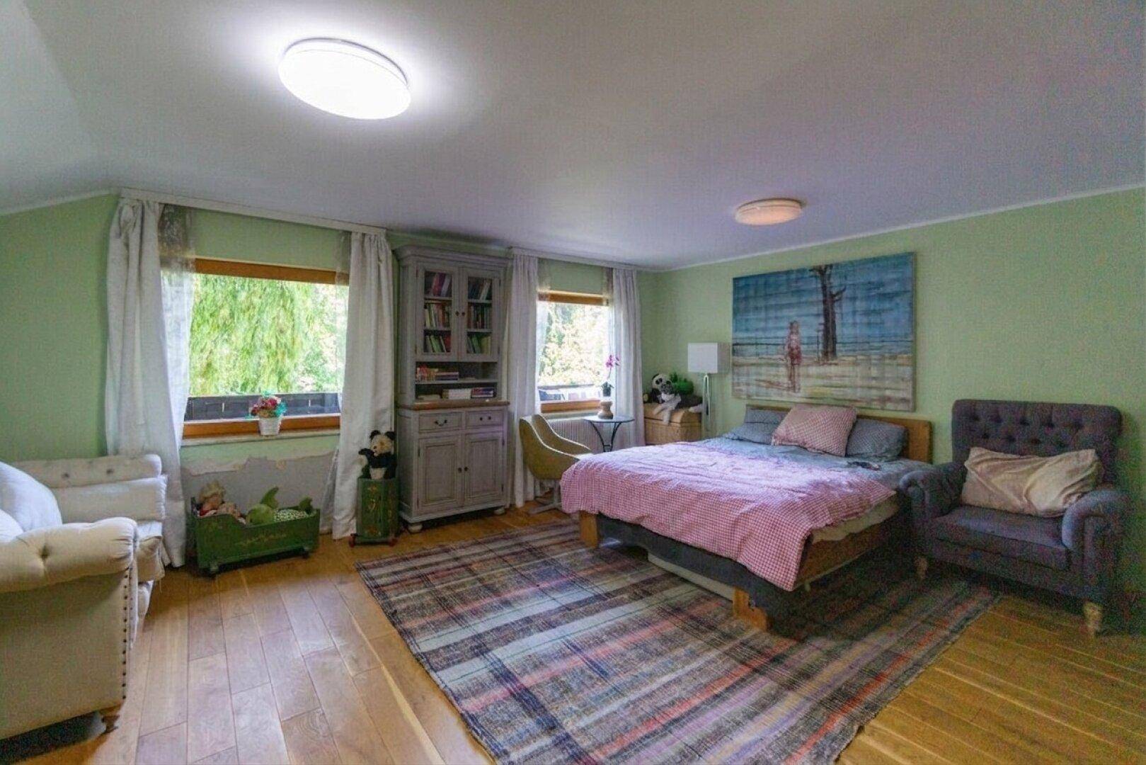 Gemütliches Schlafzimmer mit grünen Wänden, Holzboden und großen Fenstern mit Blick ins Grüne.