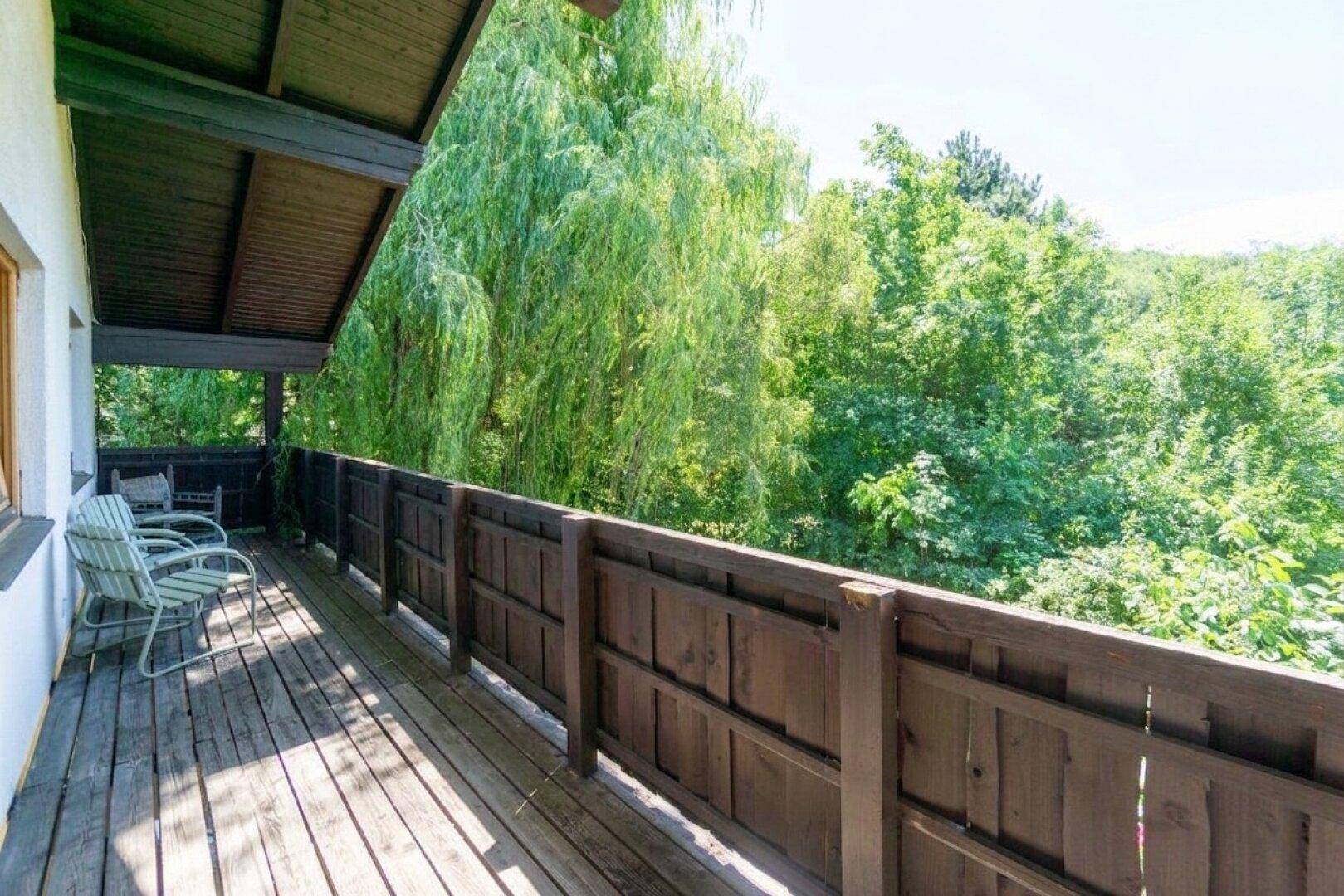 Geräumiger Holzbalkon mit Sitzgelegenheiten und weitem Blick auf die umliegende grüne Landschaft.