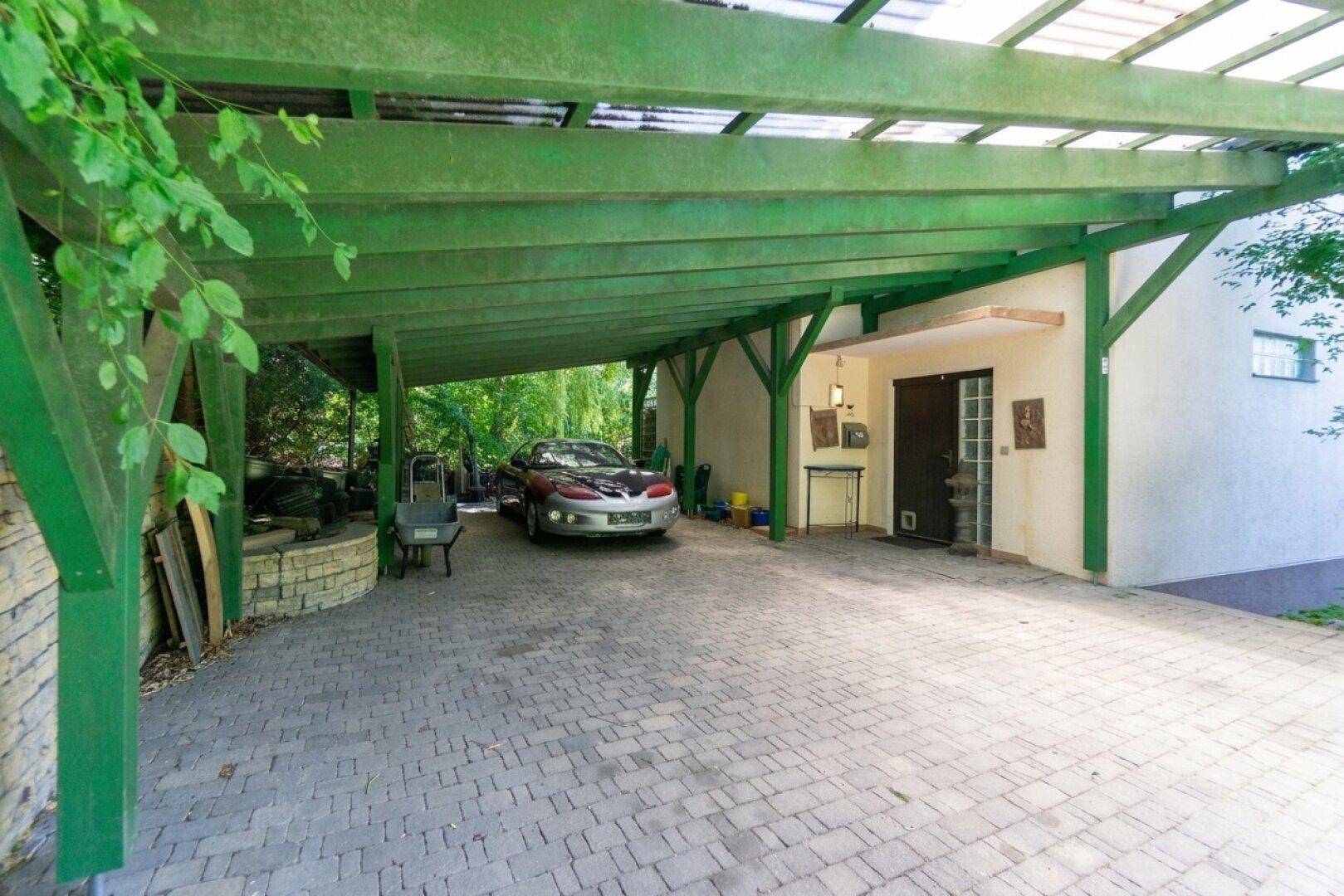 Überdachter Carport-Bereich mit gepflasterter Einfahrt und dem Haupteingang des Hauses.