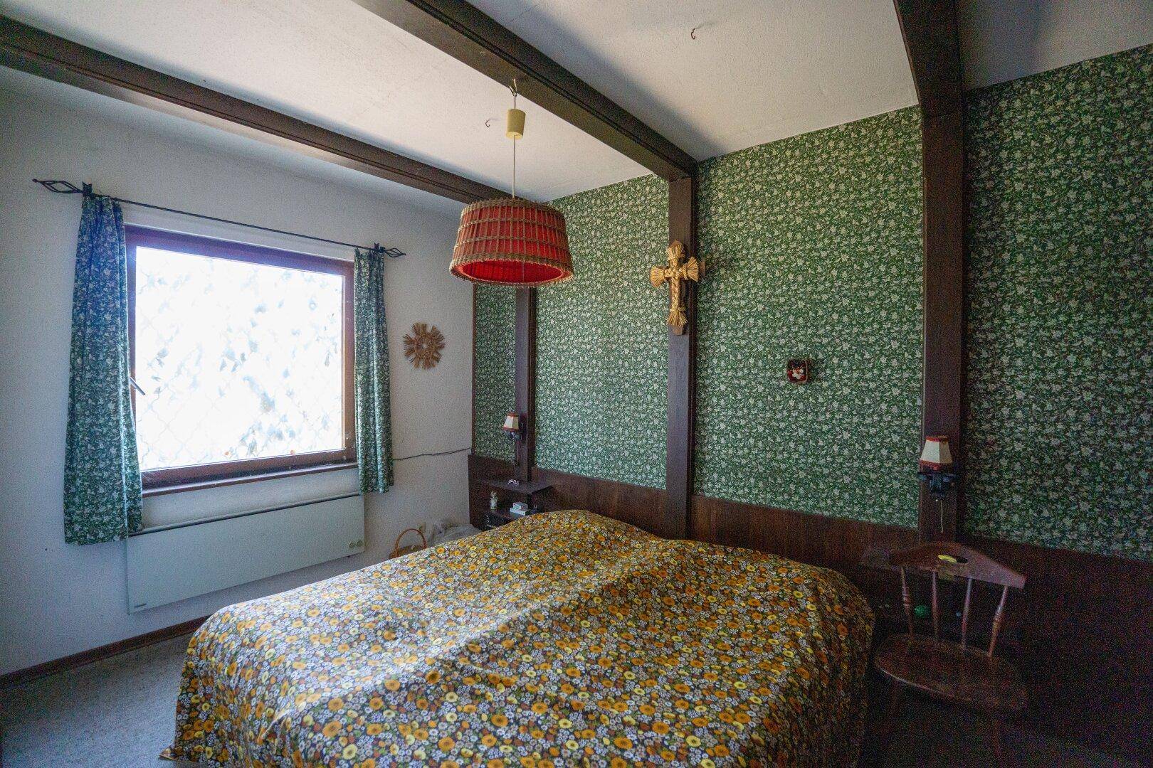 Schlafzimmer mit grüner Tapete, Holzbalken und traditioneller Einrichtung.
