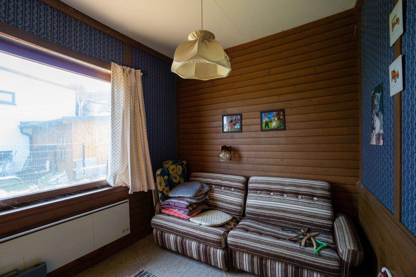 Kleines Zimmer mit Holzvertäfelung, Sofa und Fenster mit Blick nach draußen.